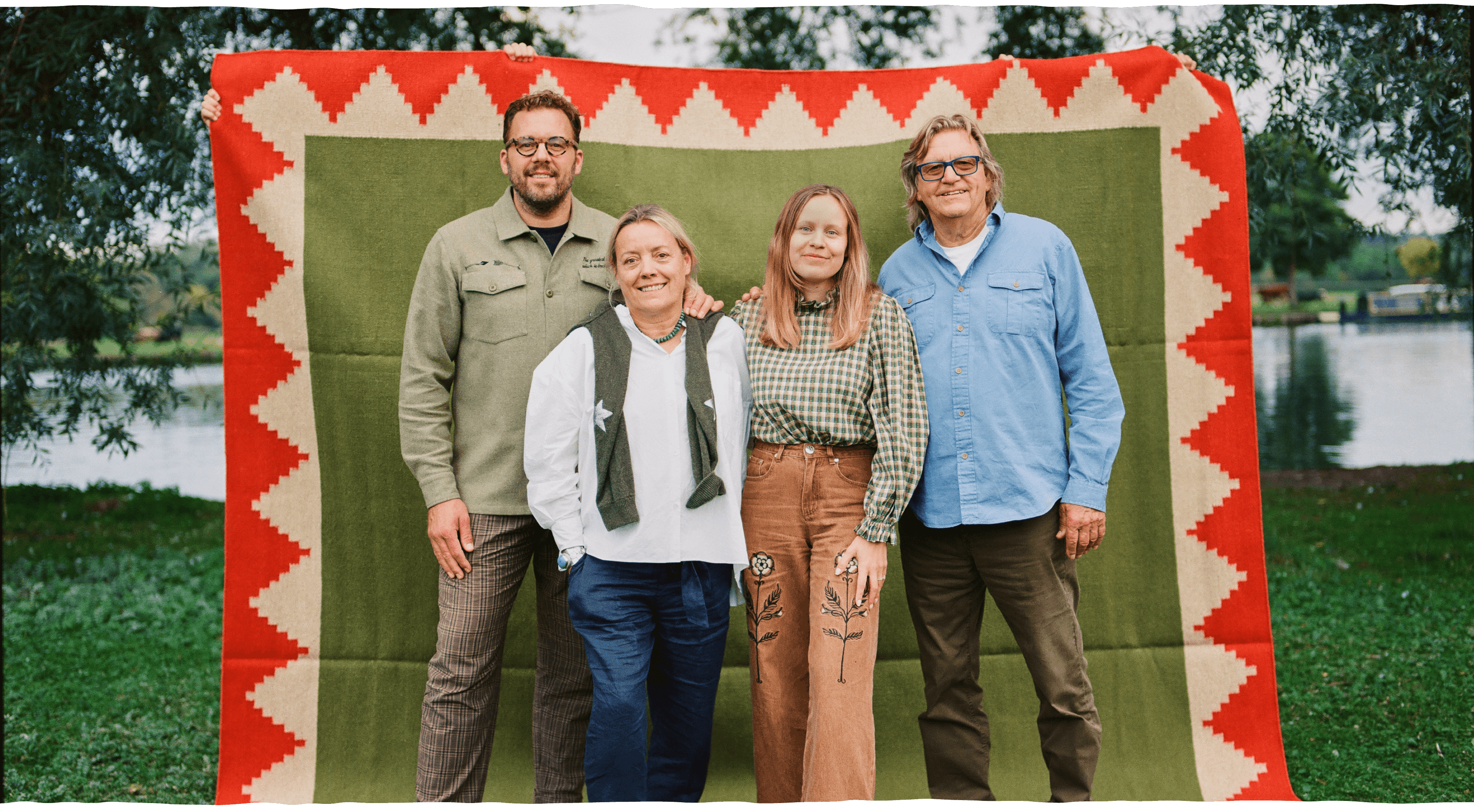 Group of four individuals standing in front of a colorful patterned textile backdrop by a riverbank