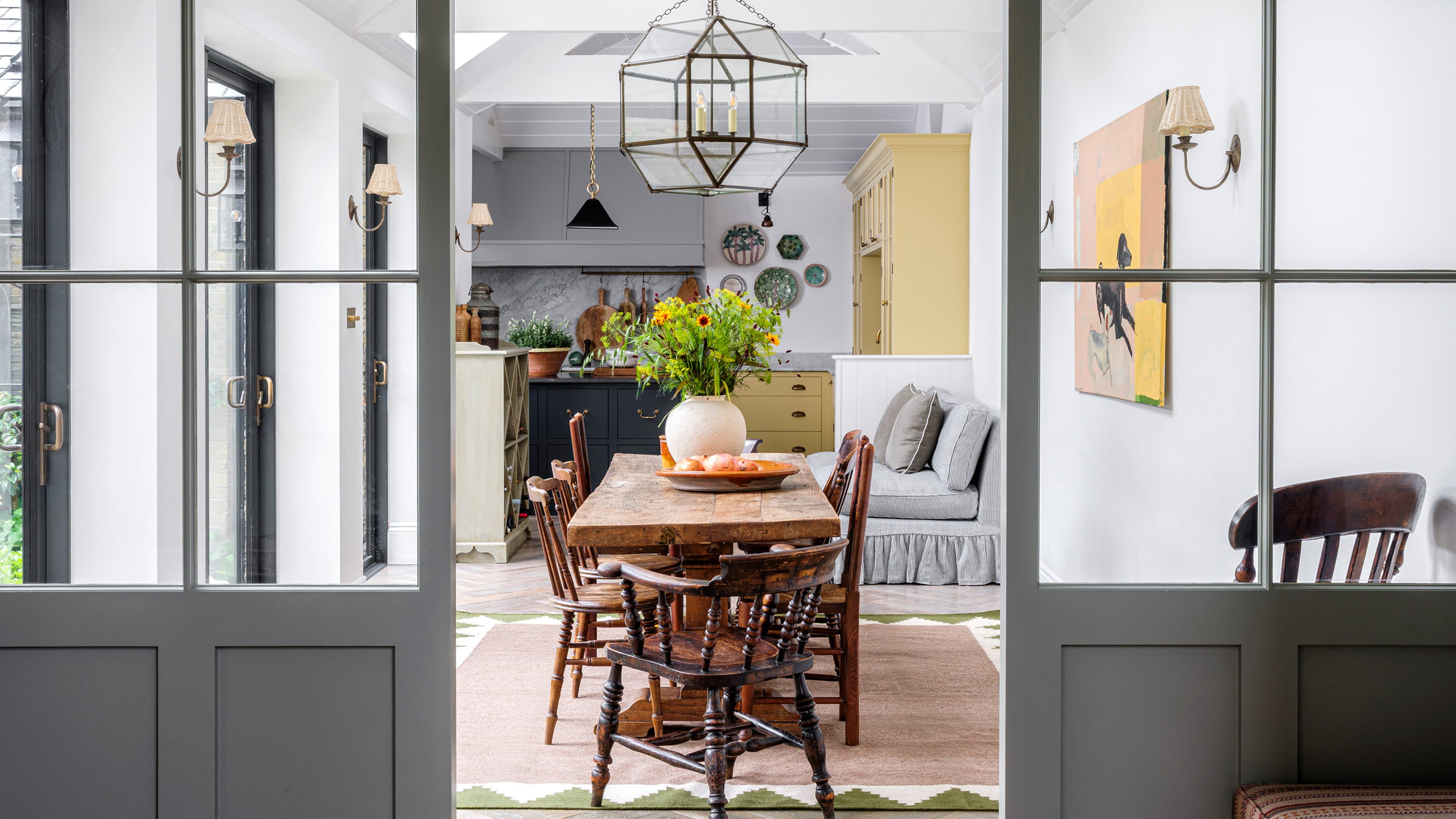Bright dining area featuring a rustic wooden table, vintage spindle chairs, and a geometric patterned rug on herringbone oak flooring