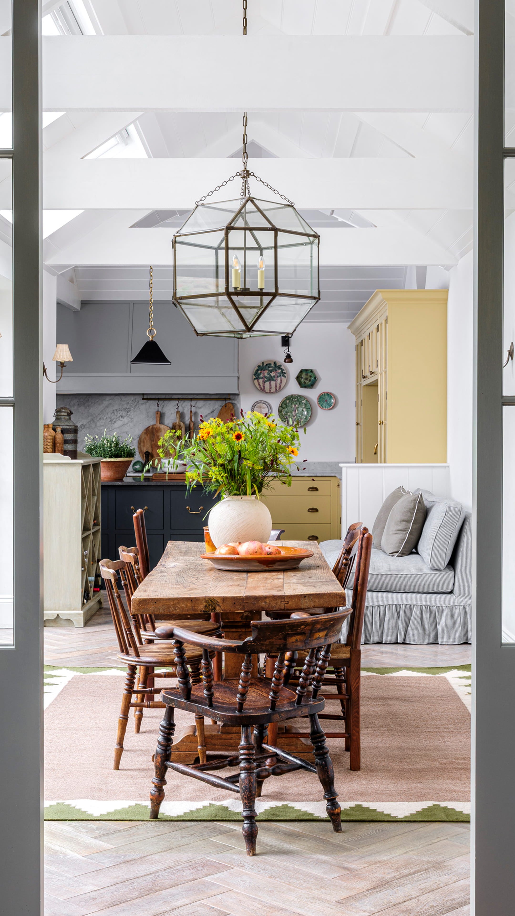 Bright dining area featuring a rustic wooden table, vintage spindle chairs, and a geometric patterned rug on herringbone oak flooring