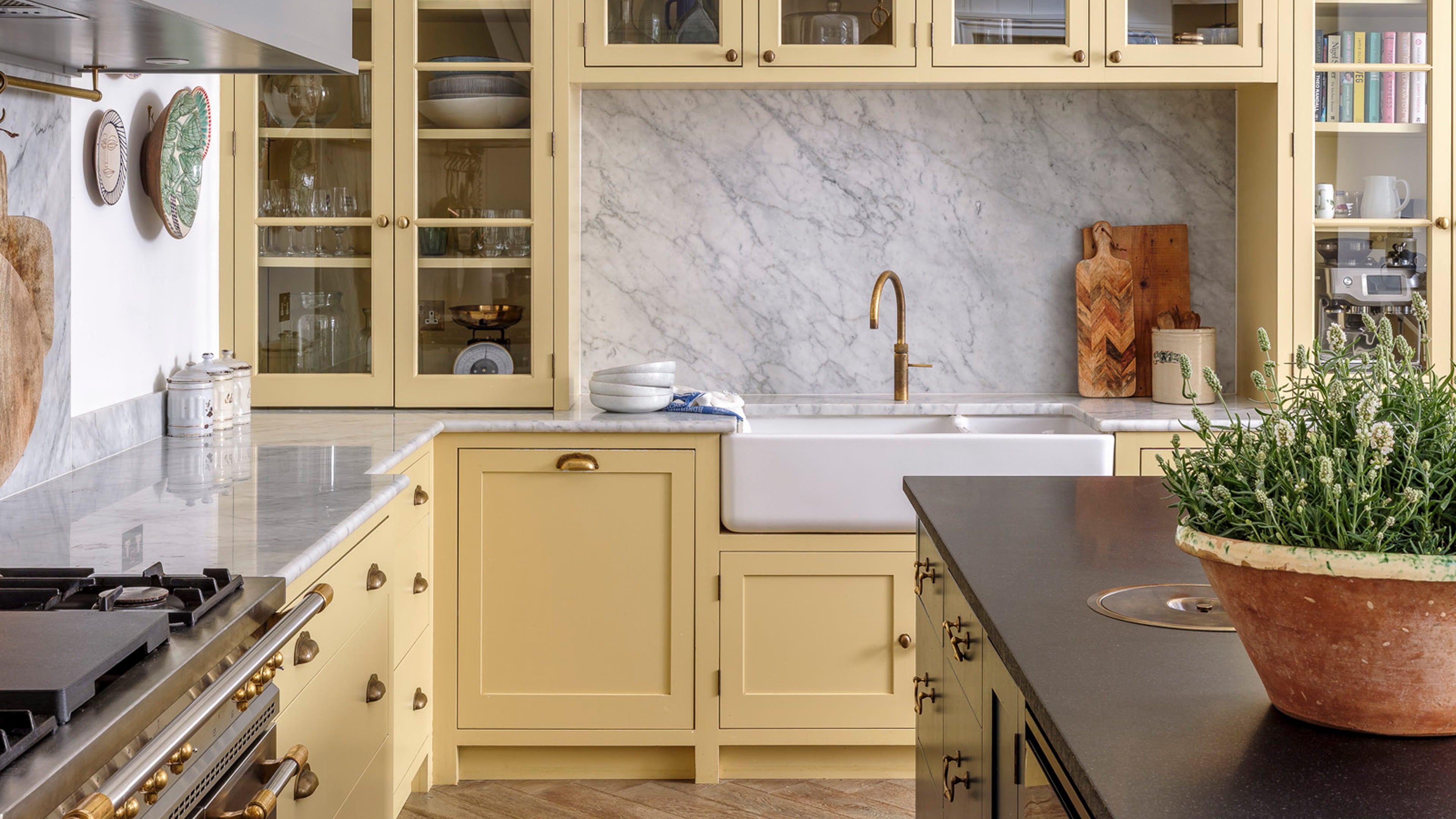 Kitchen featuring soft yellow cabinetry, a white farmhouse sink, and a striking marble backsplash with brass fixtures