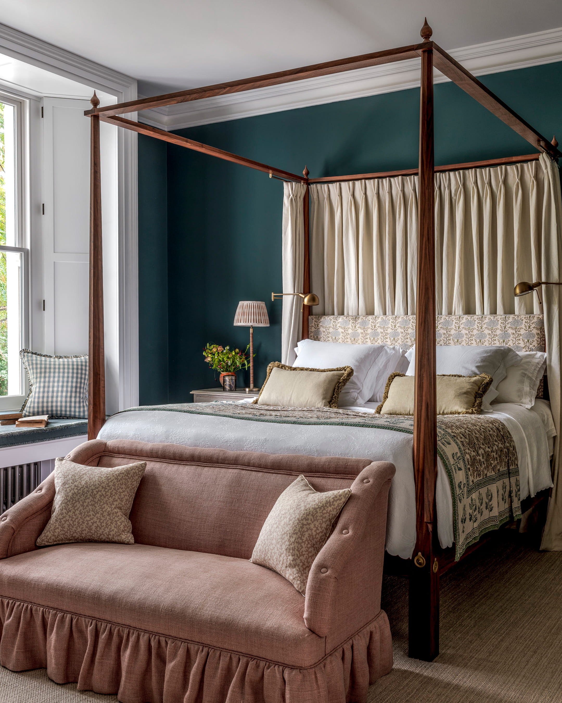 Canopied bed with dark walnut posts, deep teal walls, and a pink linen settee adorned with floral cushions