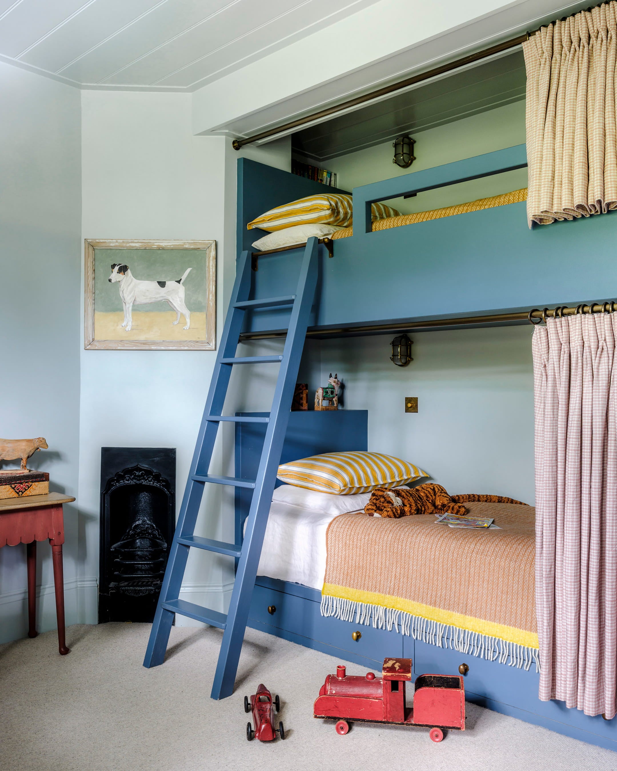 Child's bedroom featuring a blue bunk bed with striped yellow and white cushions, a vintage dog painting, and a red toy train
