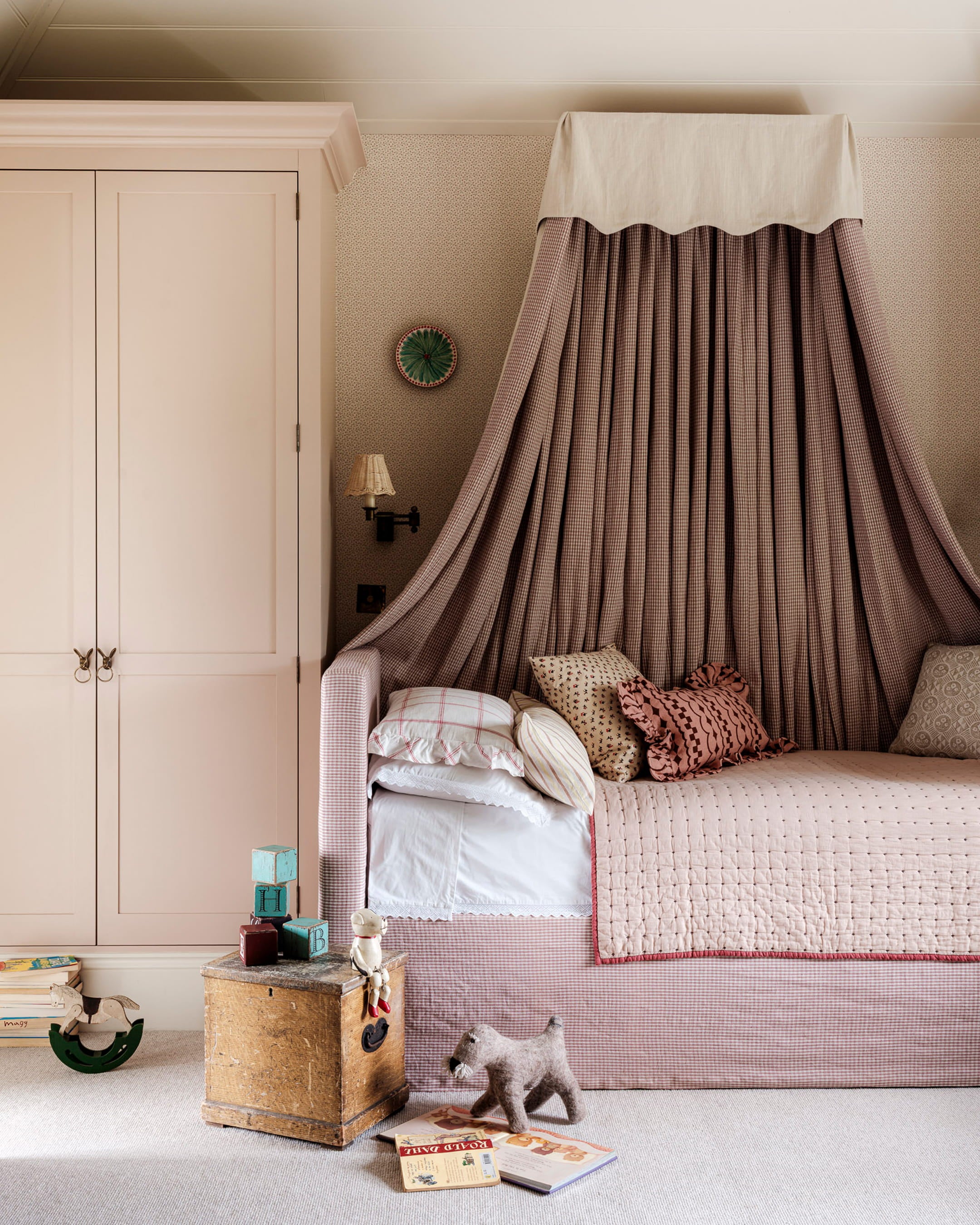 Cozy bedroom featuring a pink gingham bed with a fabric canopy, vintage storage box, and decorative patterned cushions