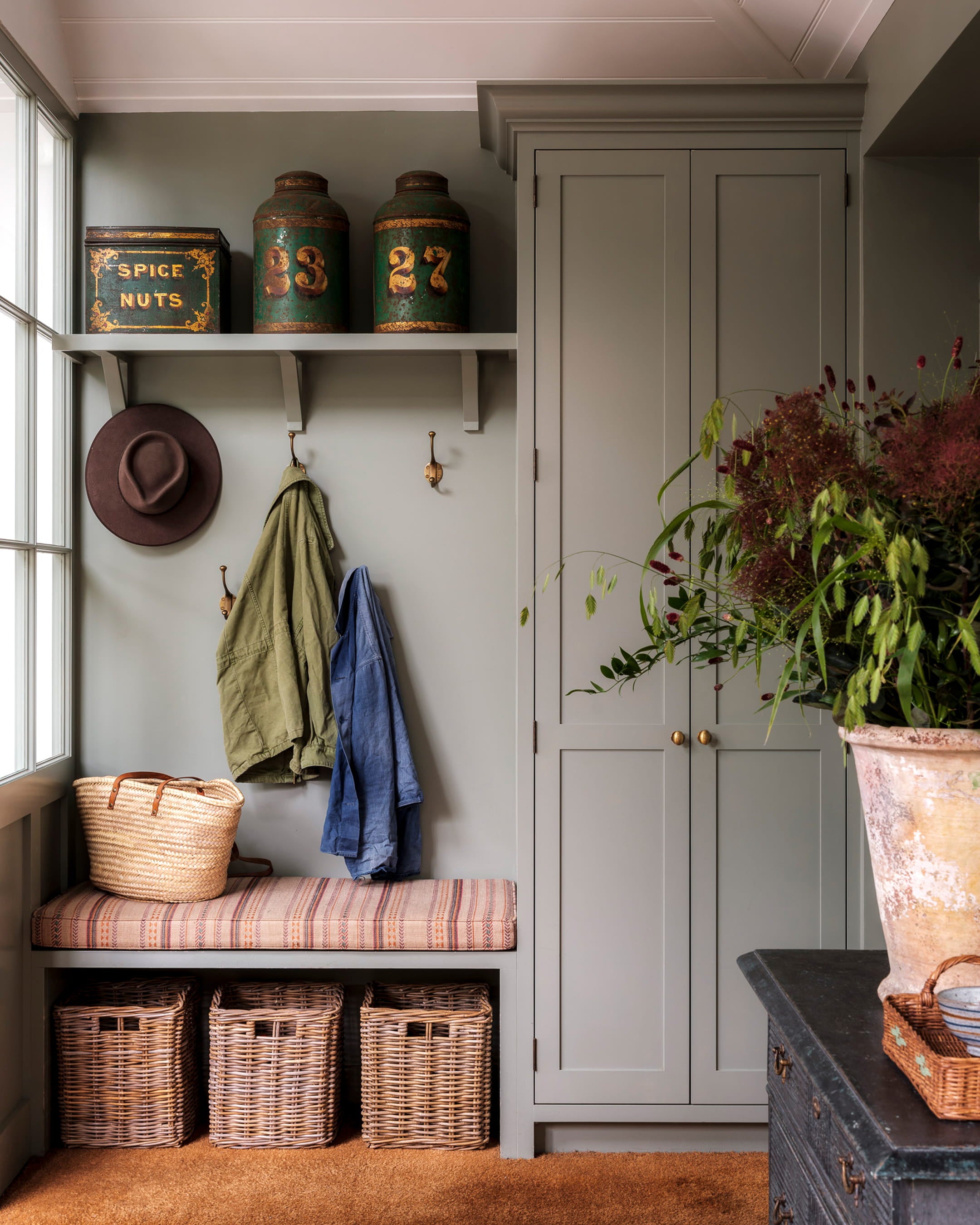 Mudroom featuring soft sage green cabinetry, a striped bench cushion, and vintage storage canisters on a wooden shelf