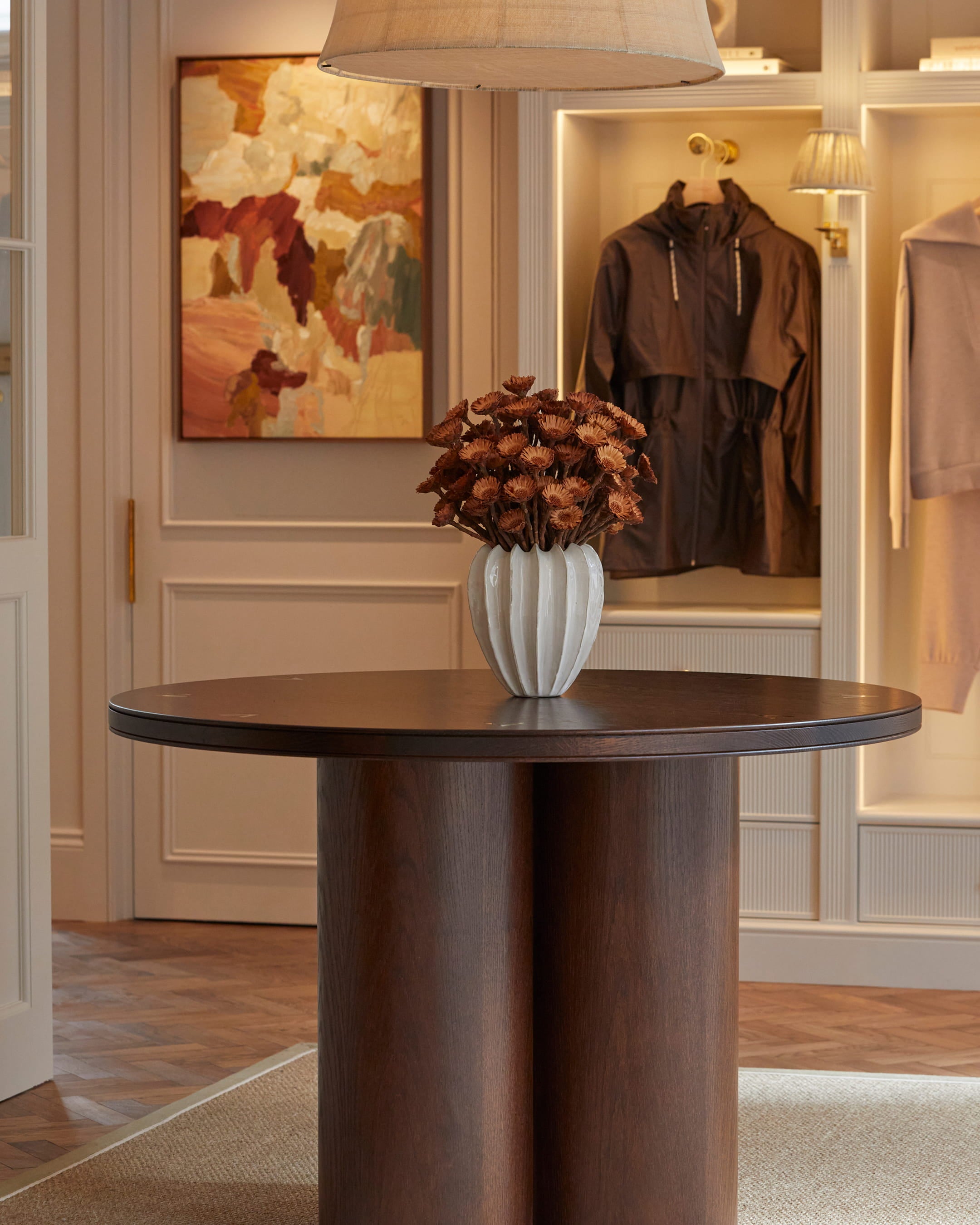 Warm ivory walls complement a dark walnut round table, topped with a textured white vase holding dried flowers, in a stylish entryway