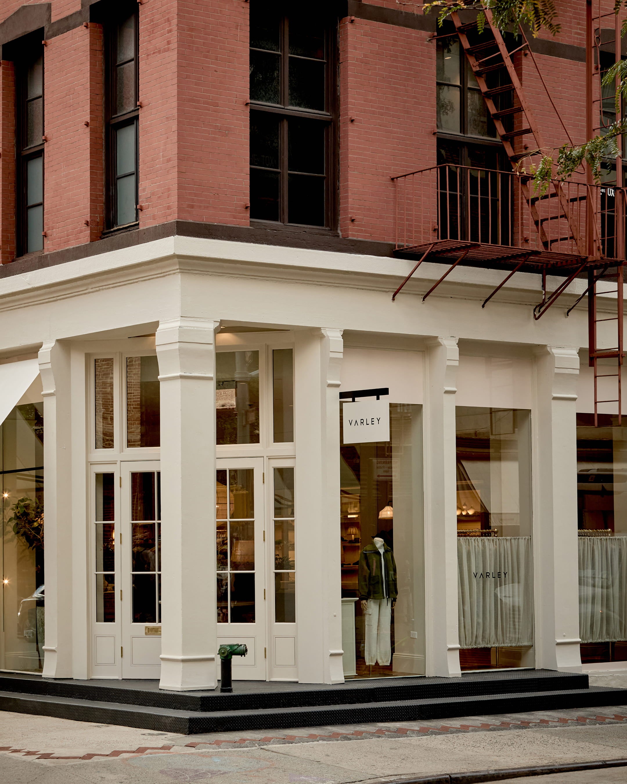 Corner storefront featuring white-painted columns, large glass windows, and a modern black sign against a red brick facade