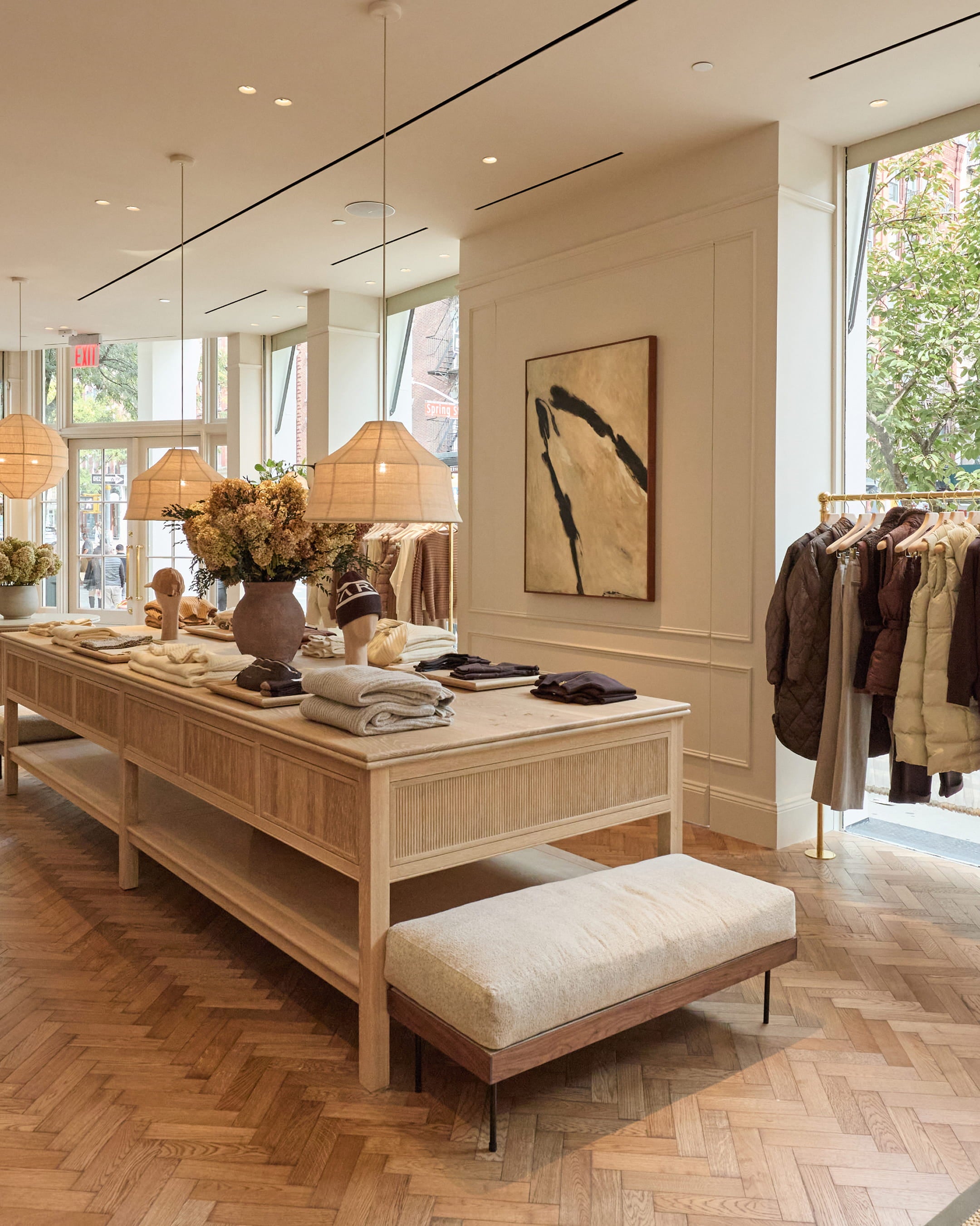 Boutique interior featuring a light oak display table, woven pendant lights, and herringbone oak flooring with minimalist decor