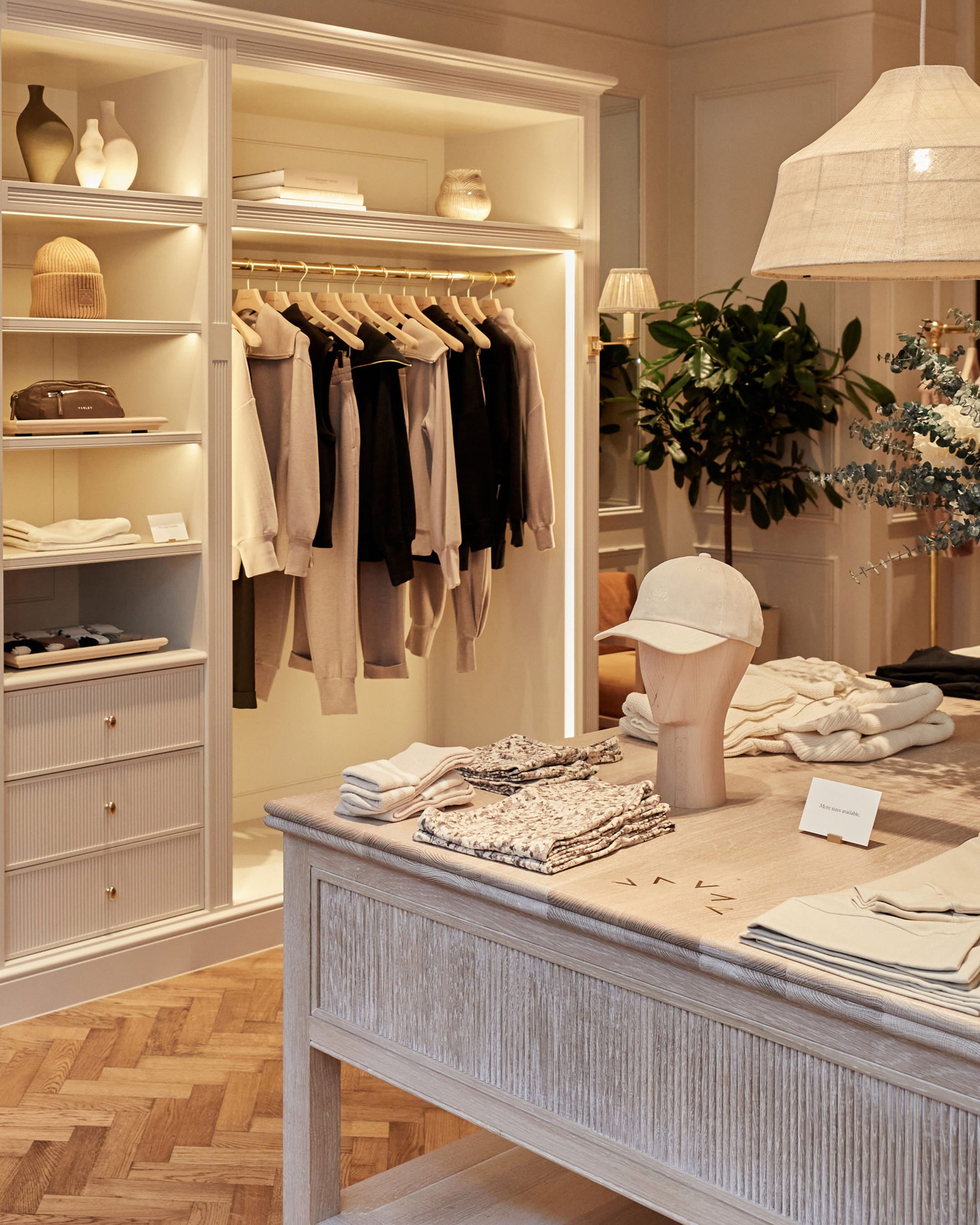 Boutique interior featuring warm ivory walls, a textured oak table, and soft grey clothing displayed on wooden hangers