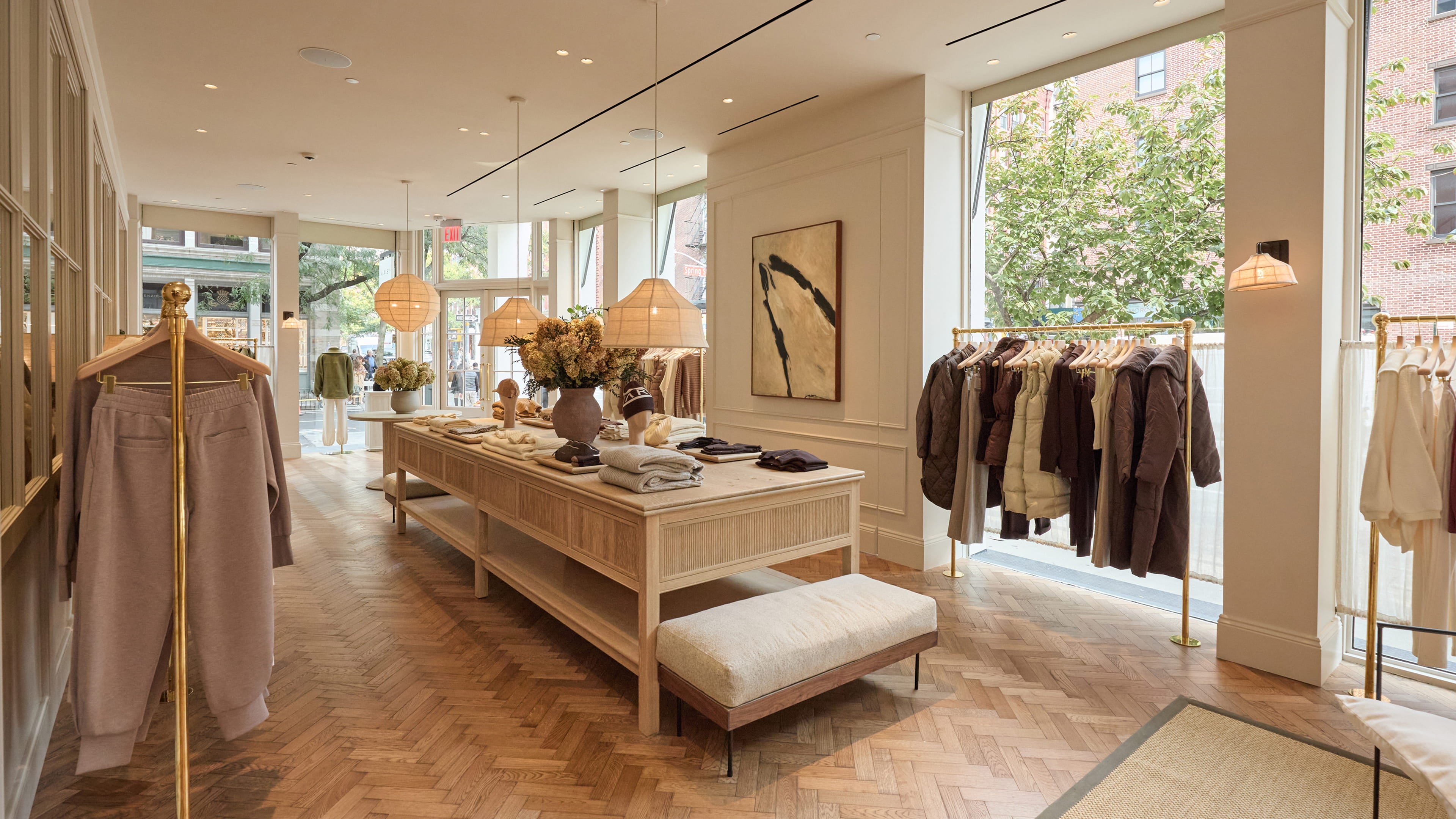 Bright retail space featuring herringbone oak flooring, a light wood display table, and woven pendant lamps with floral arrangements