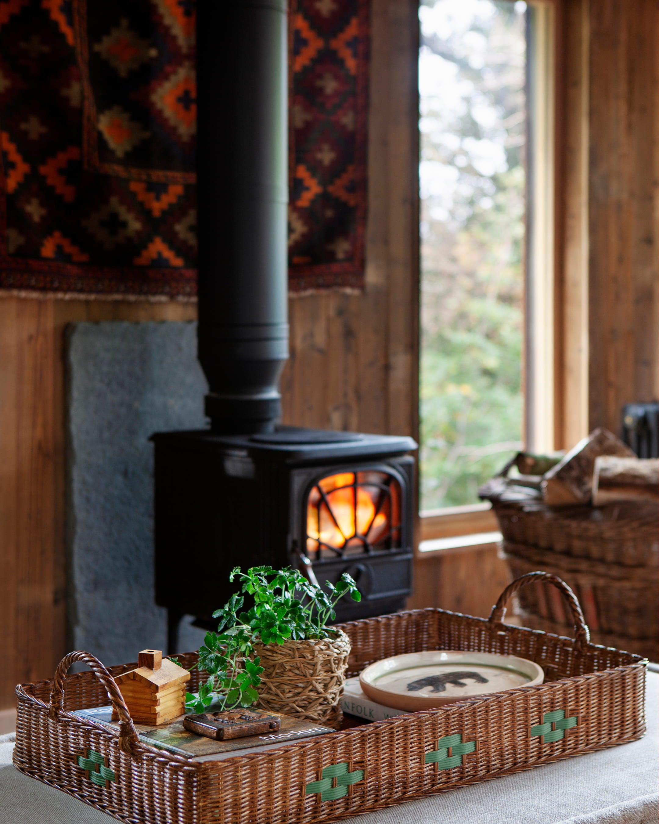 Rustic interior with warm wooden walls, a black wood-burning stove, and a woven tray holding green plants and decor items