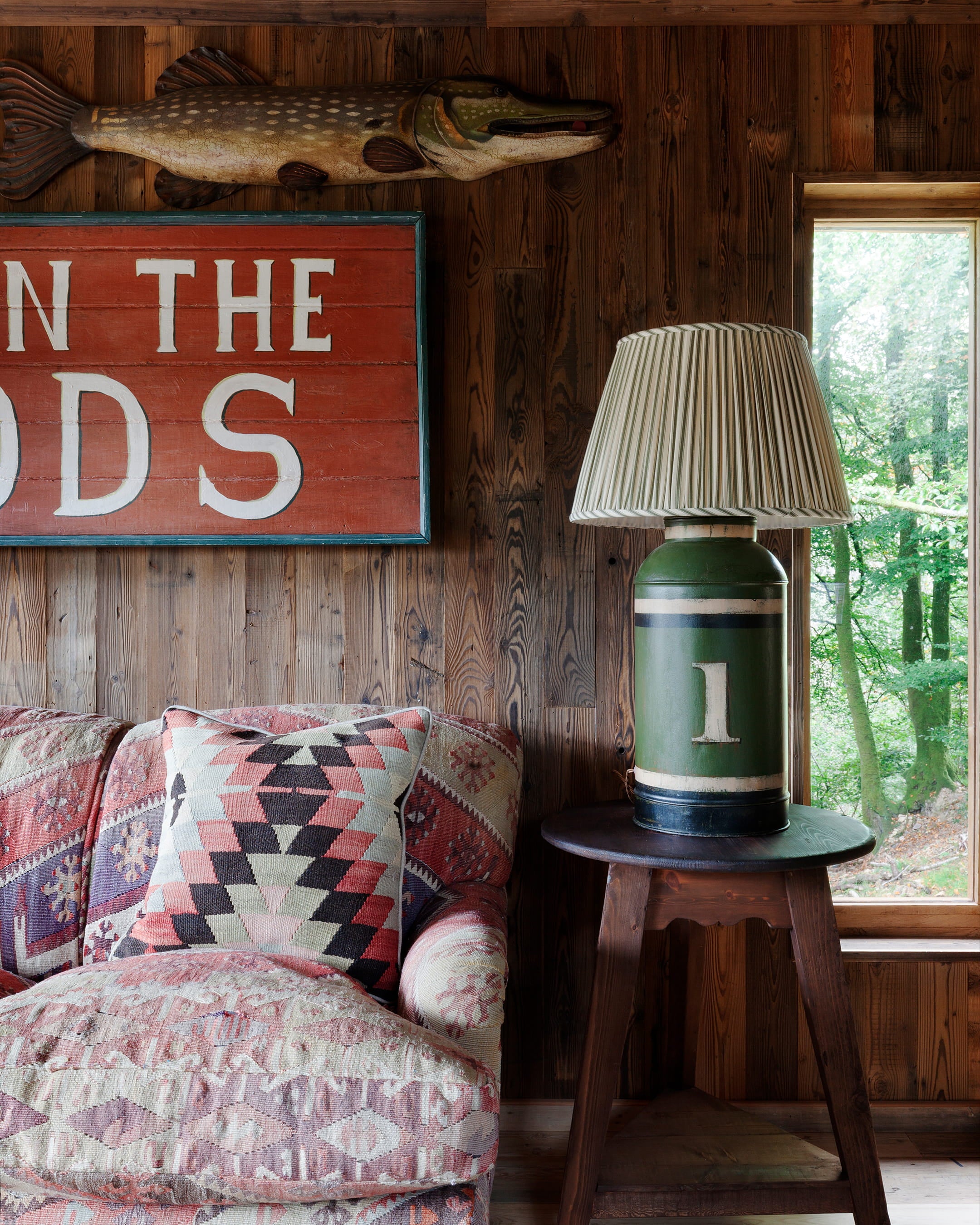 Cozy sitting area featuring a vintage patterned sofa, rustic wooden walls, and a unique green lamp with pleated shade