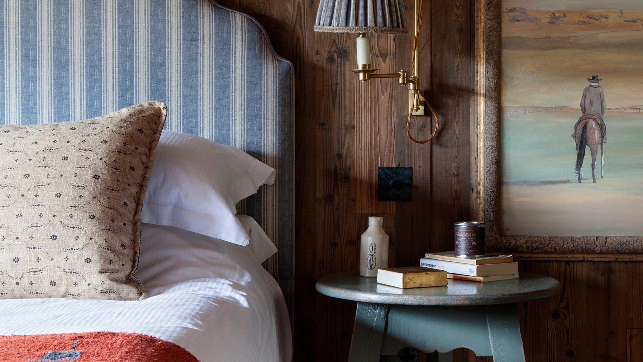 Cozy bedroom featuring a striped blue headboard, rustic wood paneling, and a warm terracotta throw blanket