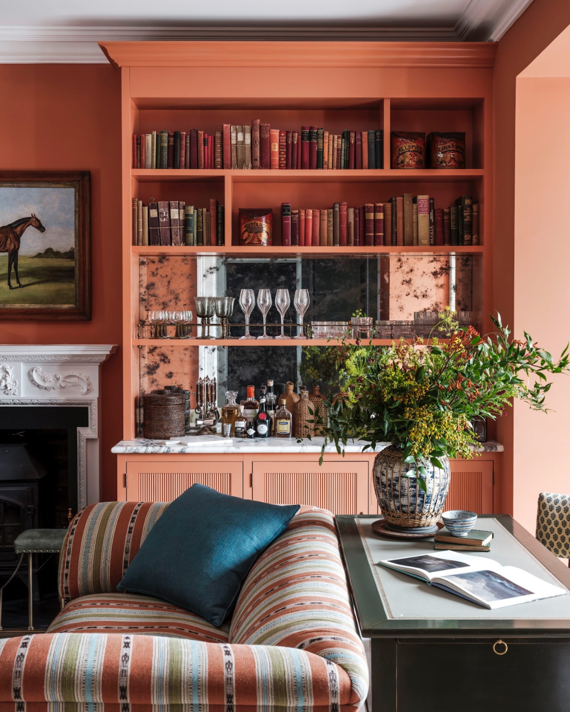 Warm terracotta walls highlight a striped sofa with earthy tones, a marble-topped bar, and vintage books on display