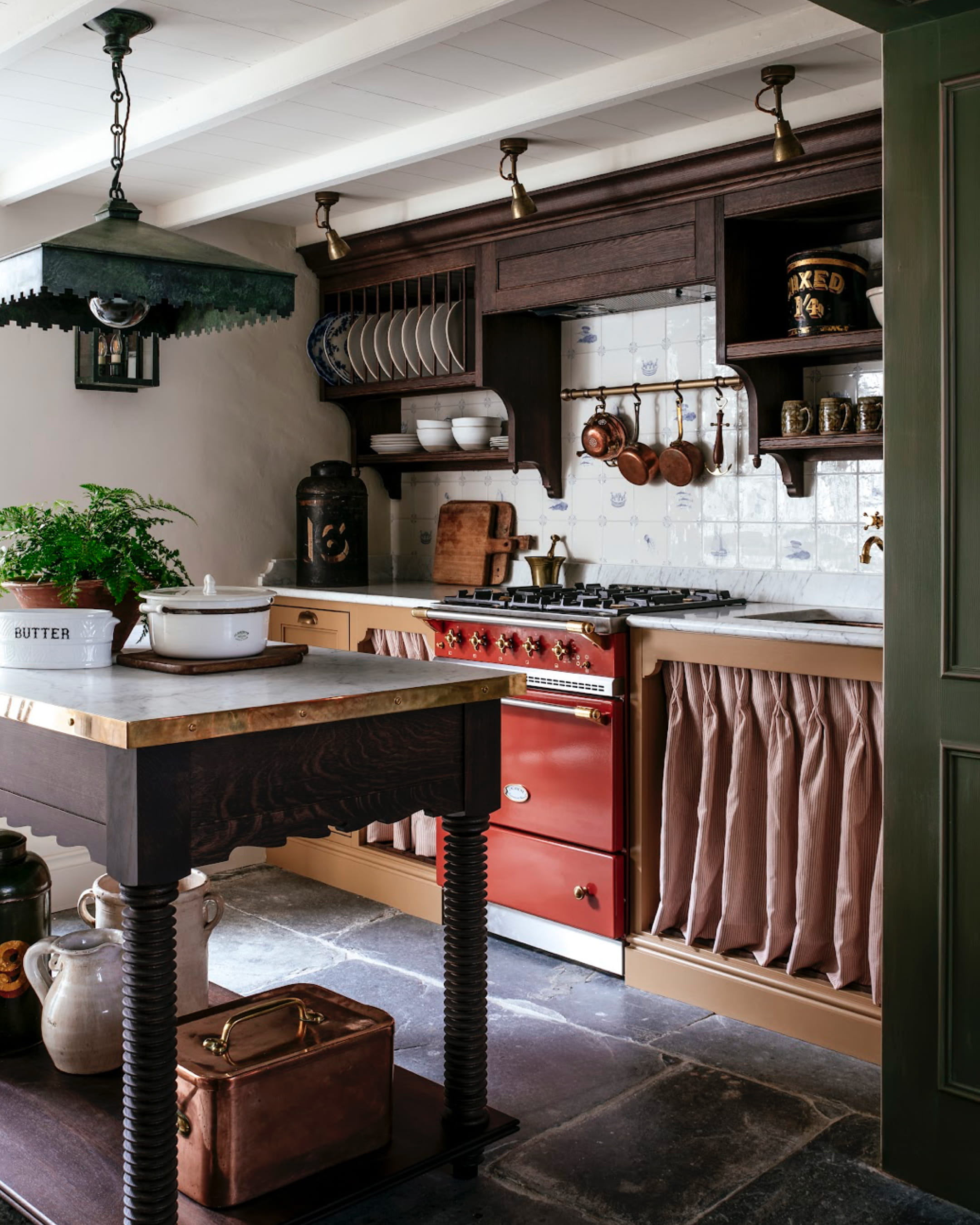 Kitchen featuring a brass range cooker, white ceramic dishware, and dark oak cabinetry with a vintage copper pot collection