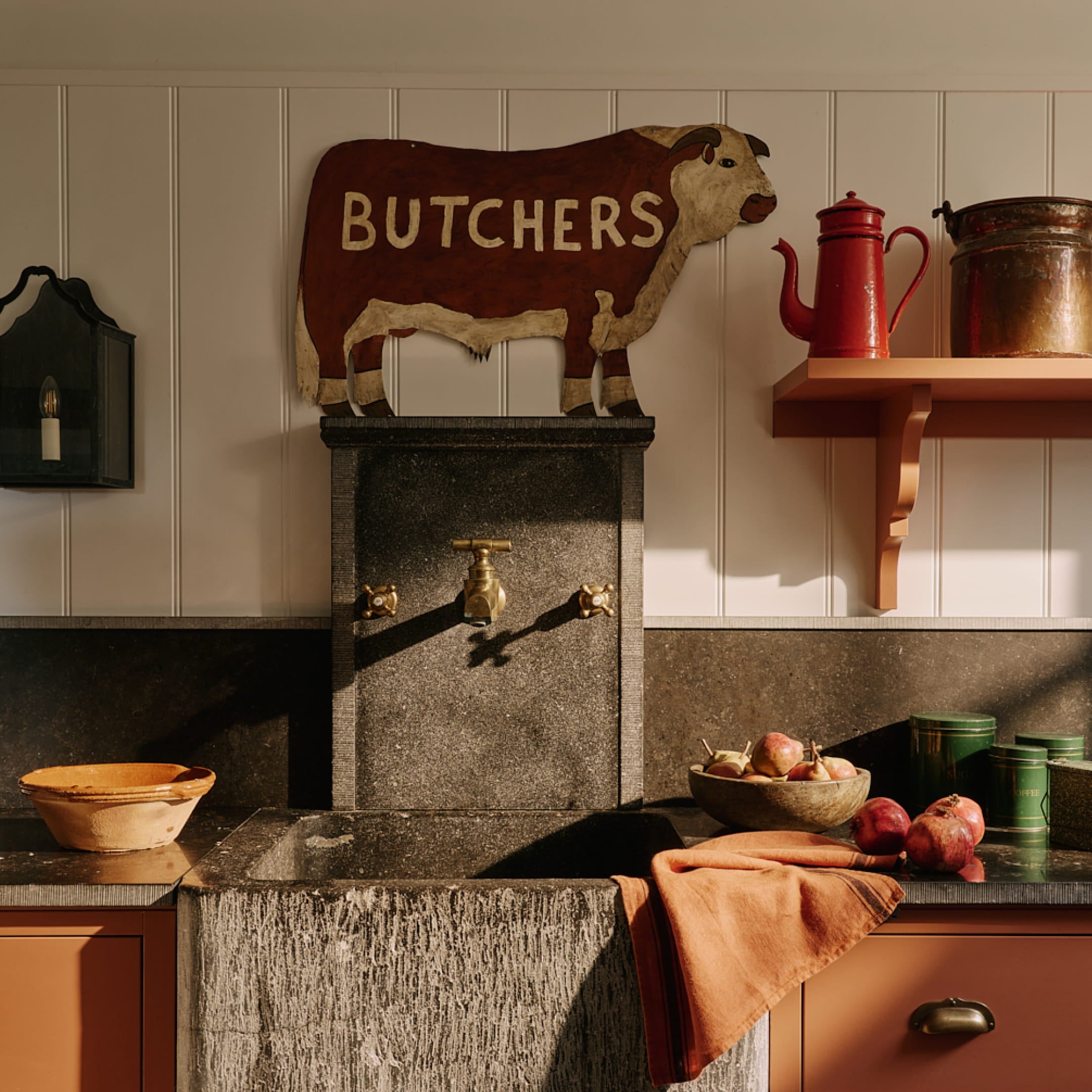Rustic kitchen featuring a black granite sink, terracotta bowl, and a vintage butcher sign above a textured stone wall