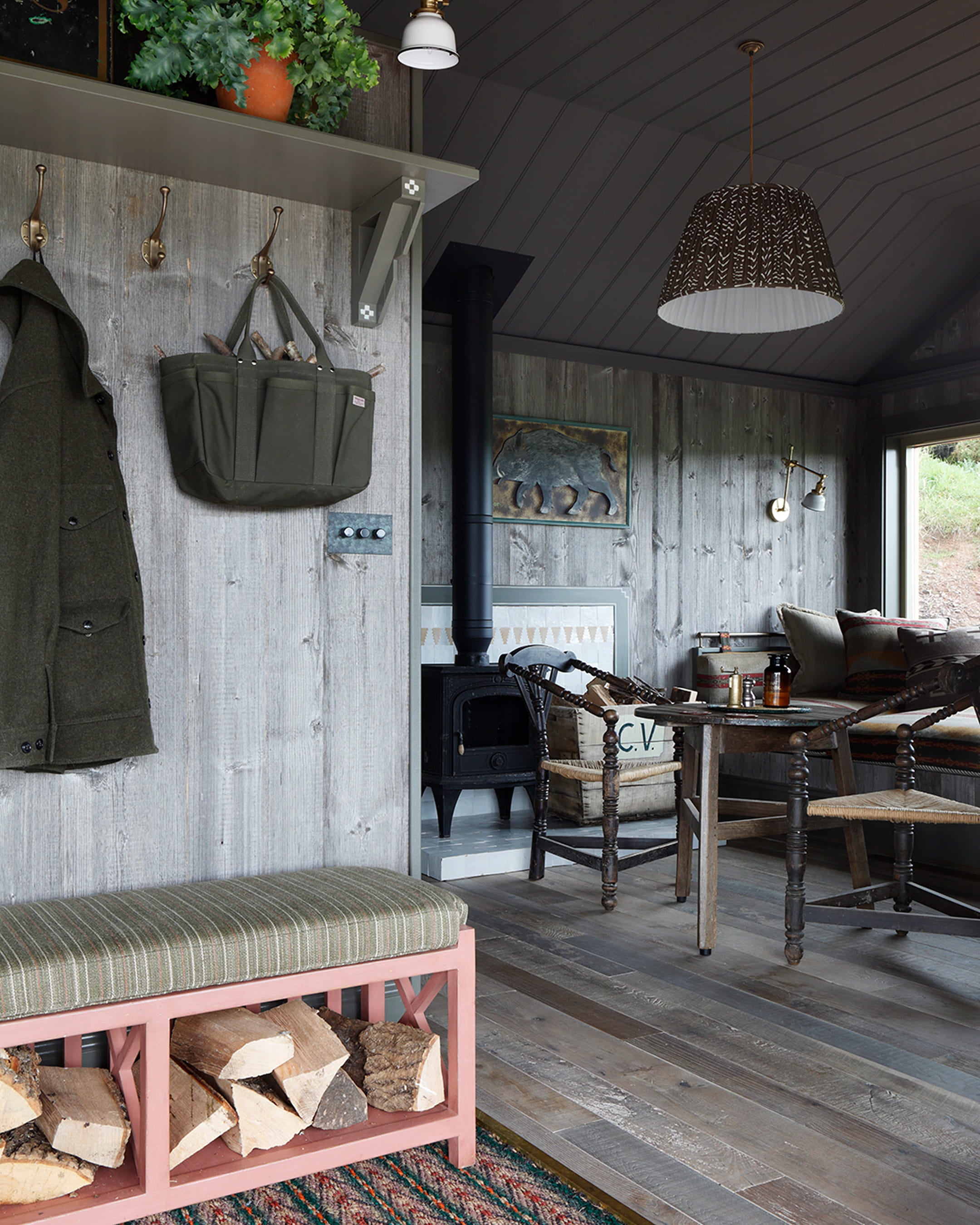 Cozy interior featuring a dark grey wooden ceiling, reclaimed wood walls, and a pink log storage bench with a striped cushion