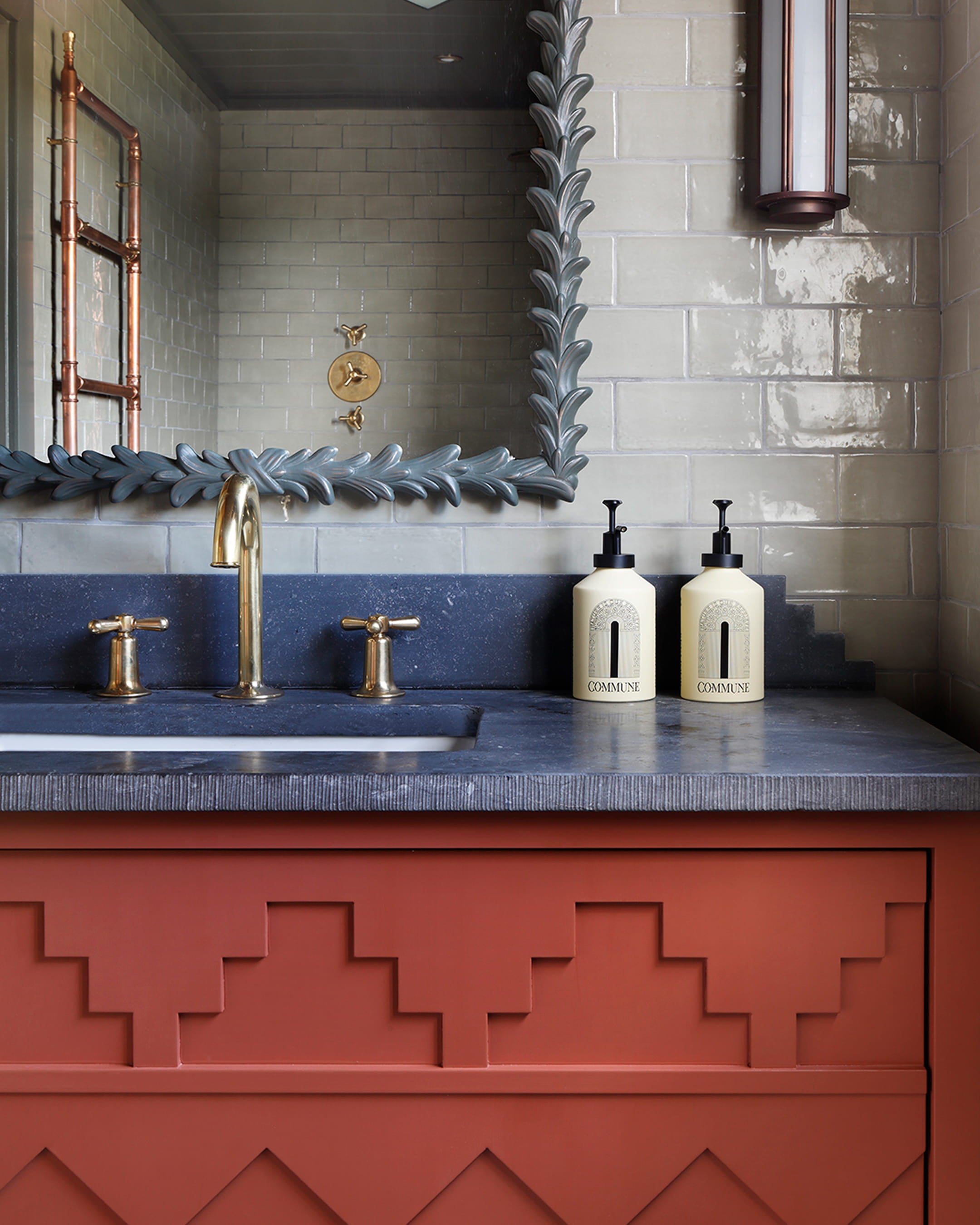 Bathroom featuring a terracotta vanity with geometric relief, navy stone countertop, and gold fixtures against glossy white tiles