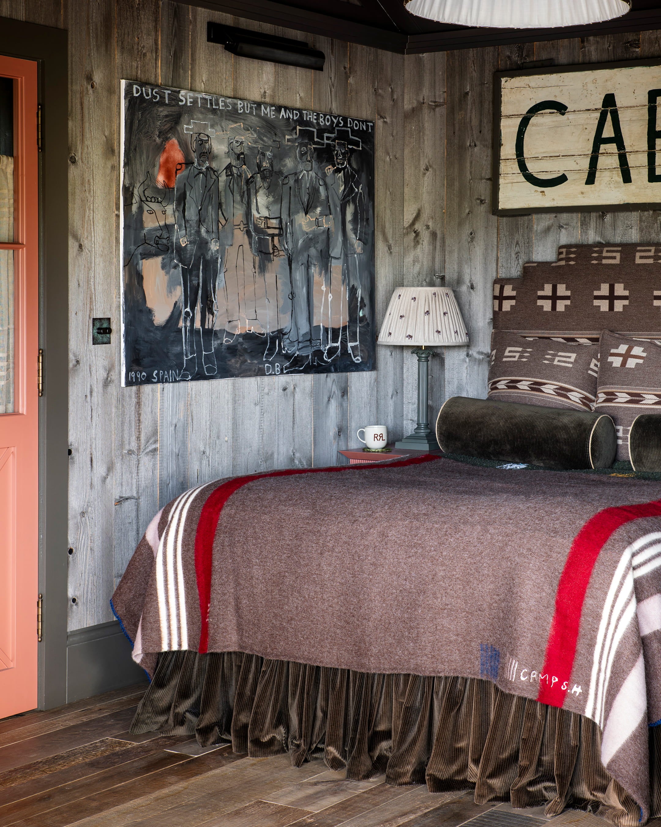 Cozy bedroom featuring a textured brown blanket, rustic wooden walls, and a striking abstract painting above the bed