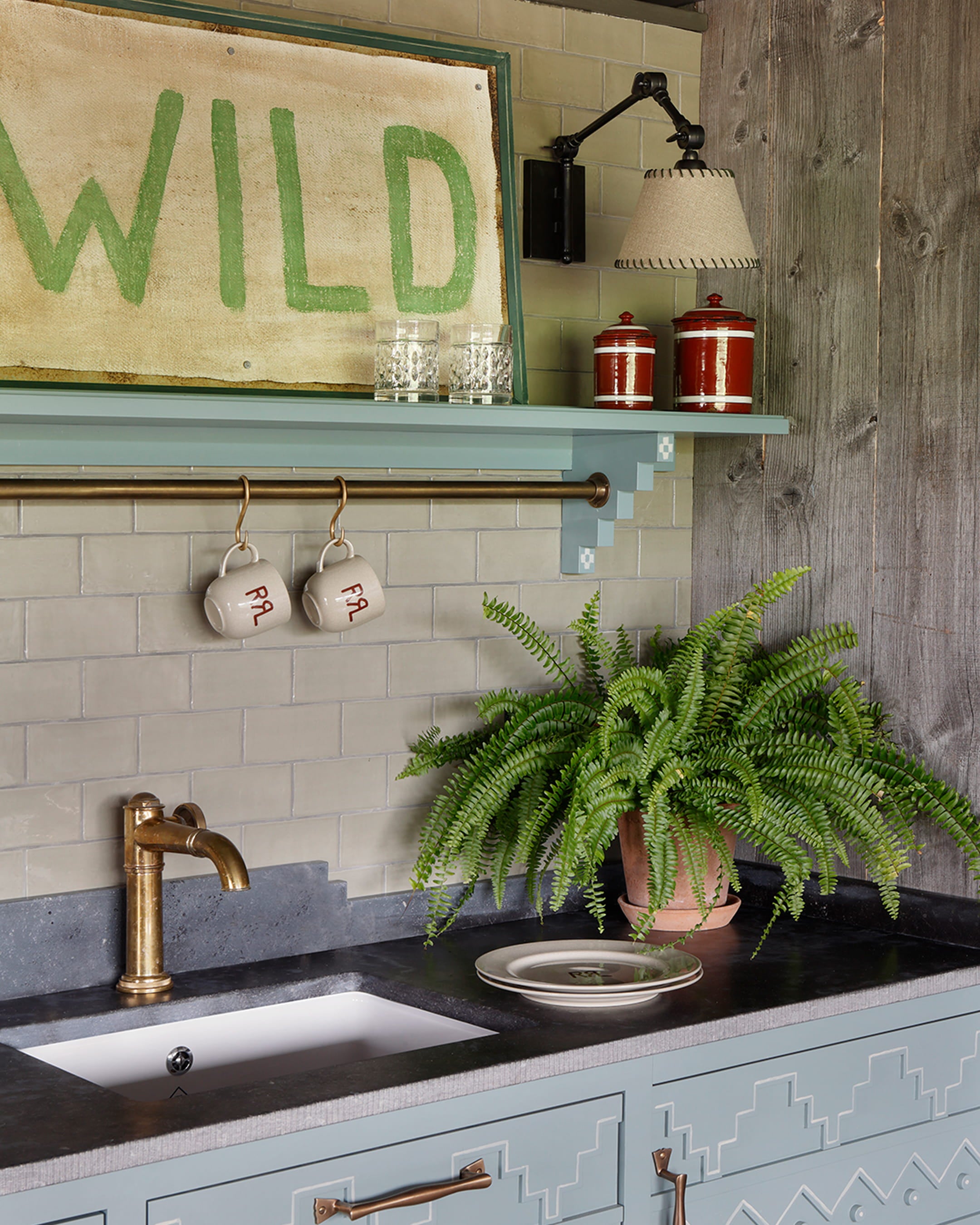 Kitchen featuring soft blue cabinetry, a dark granite countertop, gold faucet, and a vintage-inspired green sign above