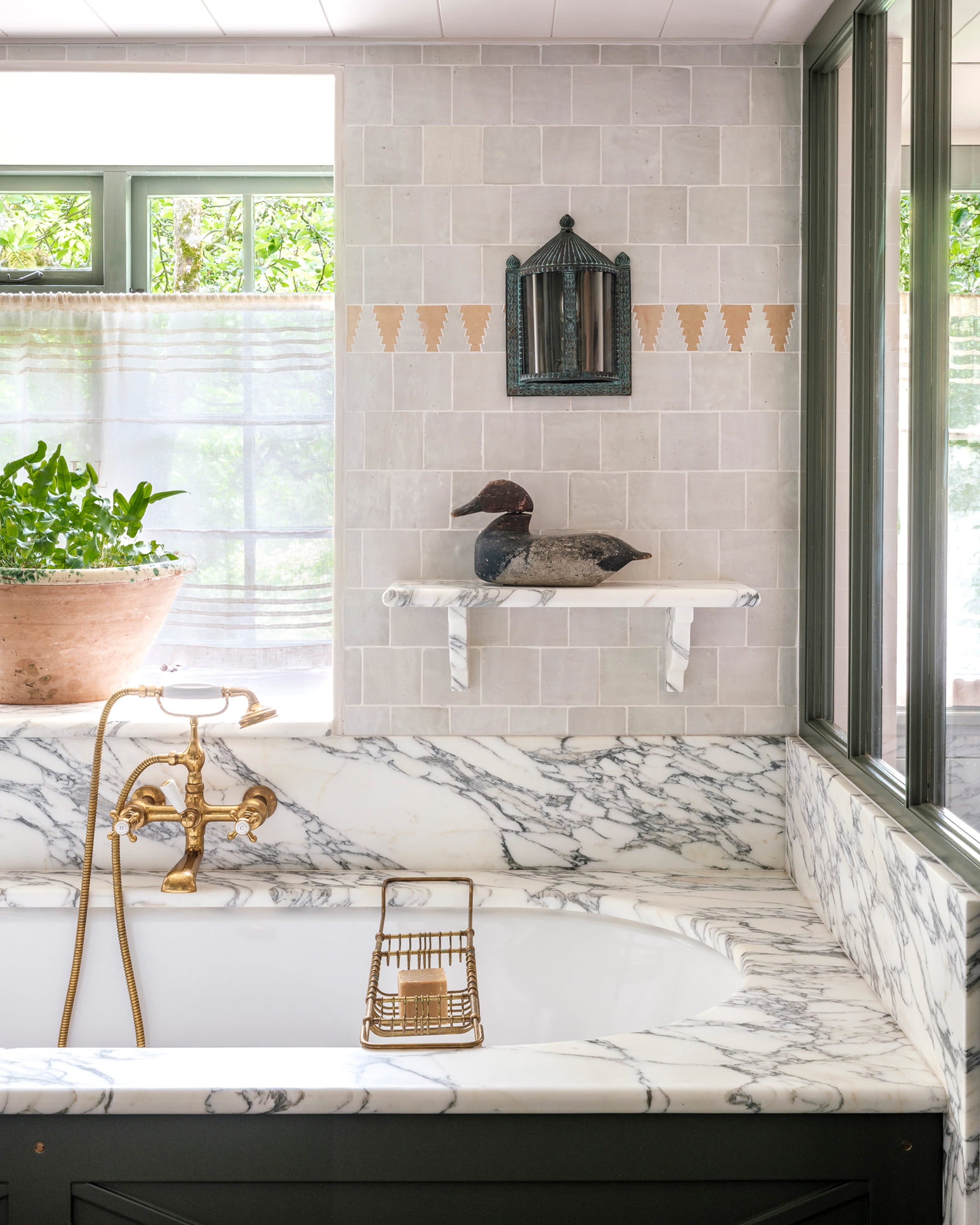 Bathroom featuring soft grey stone tiles, a white marble bathtub with a vintage brass faucet, and a rustic duck sculpture