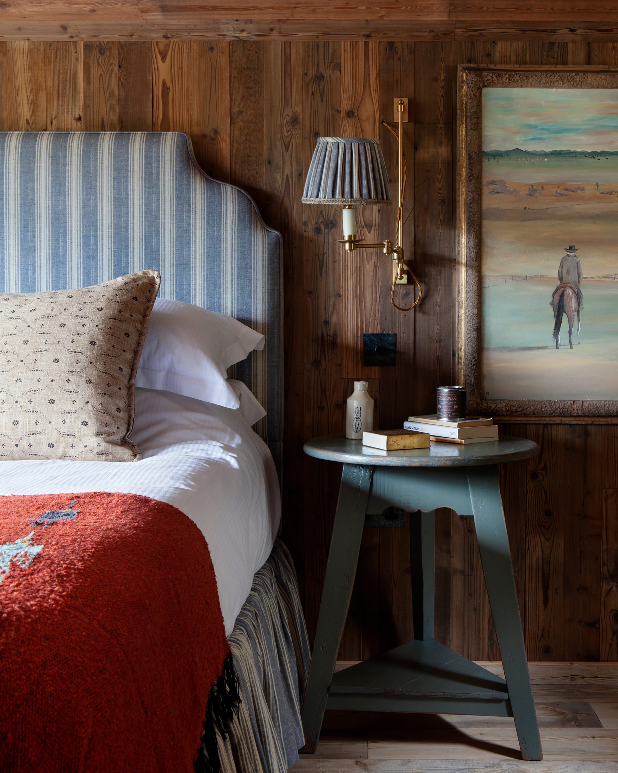 Cozy bedroom featuring a striped blue headboard, rustic wood paneling, and a warm terracotta throw blanket