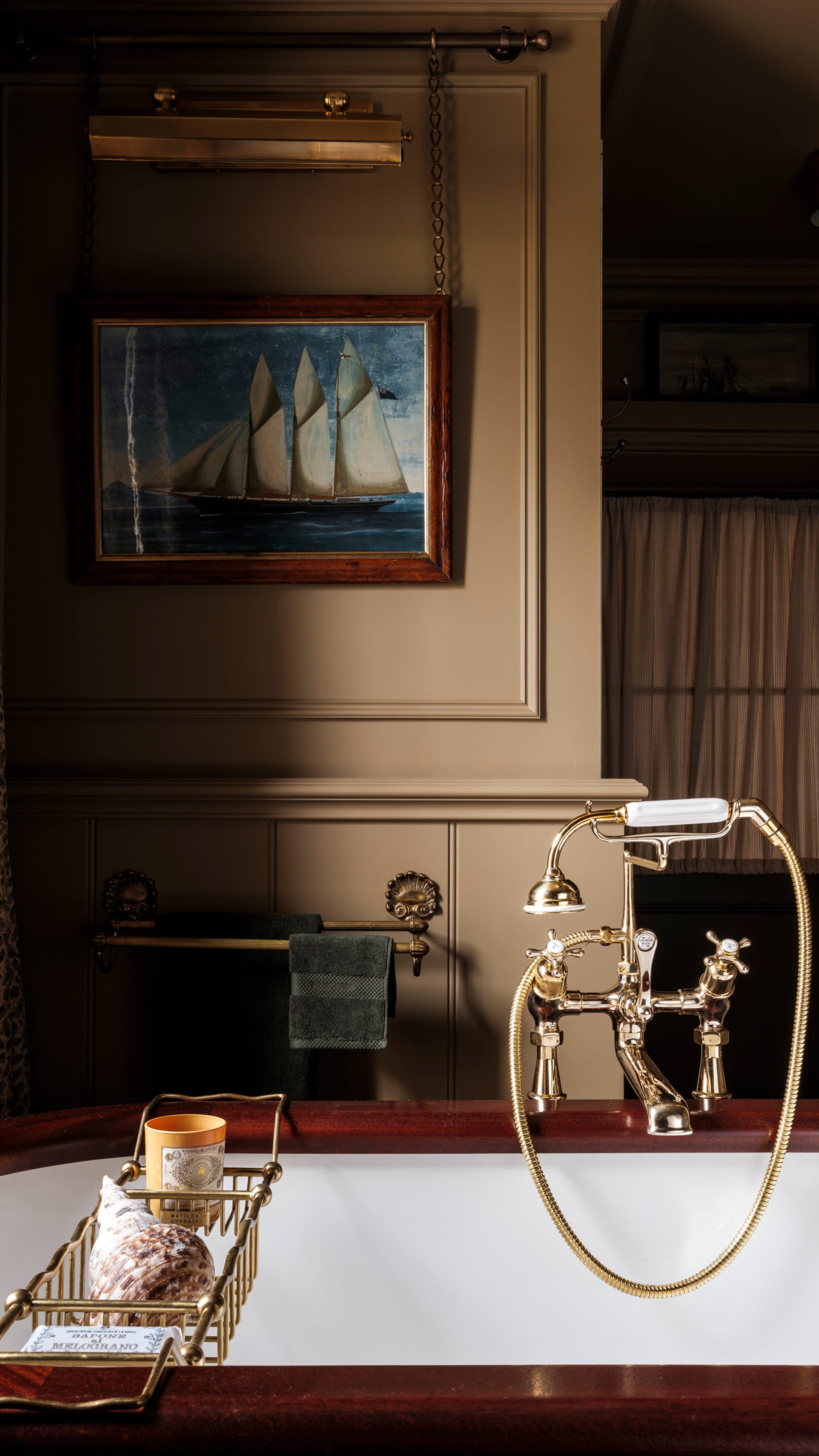 Luxurious bathroom featuring a deep mahogany tub, brass fixtures, and a vintage nautical painting above the sink