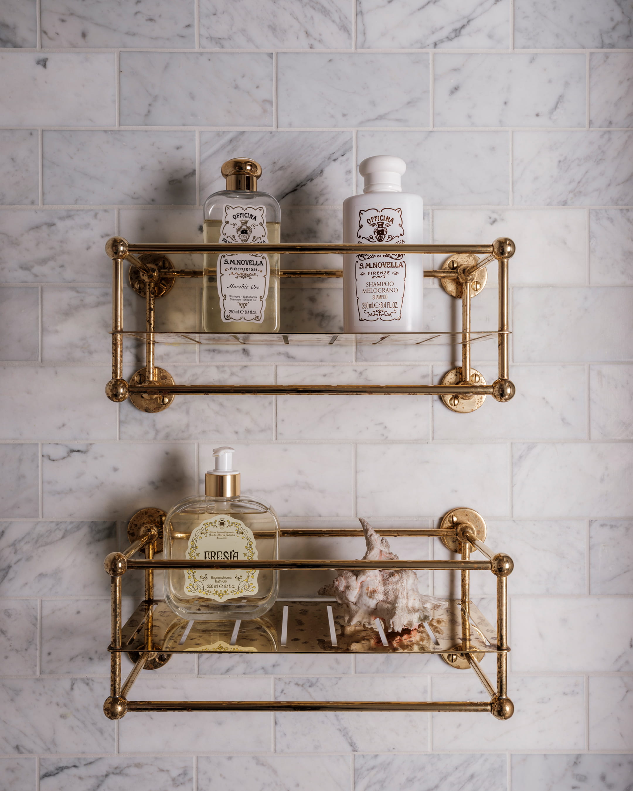 Brass shelving with vintage toiletries against a white marble tiled wall, featuring a decorative seashell accent
