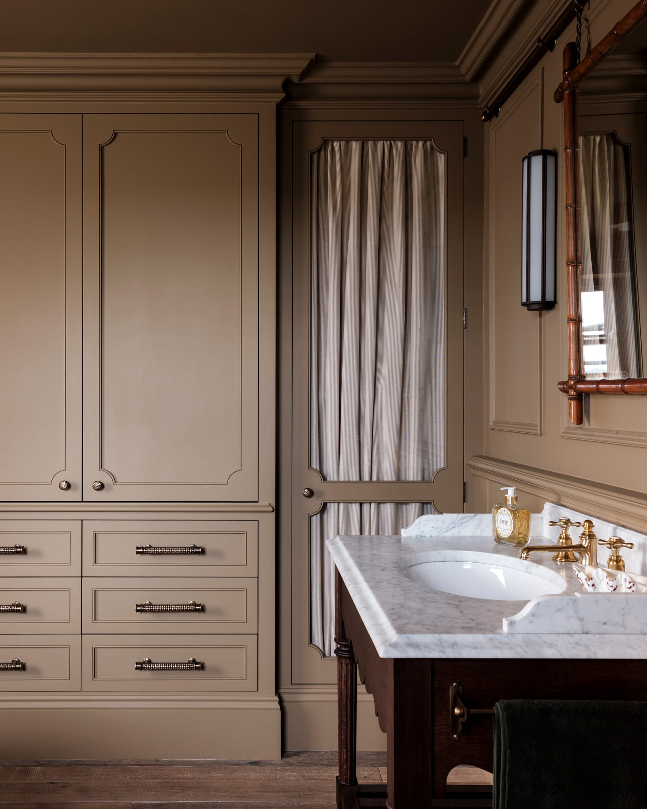 Bathroom featuring warm taupe cabinetry, a marble countertop, and brass fixtures alongside textured linen drapery