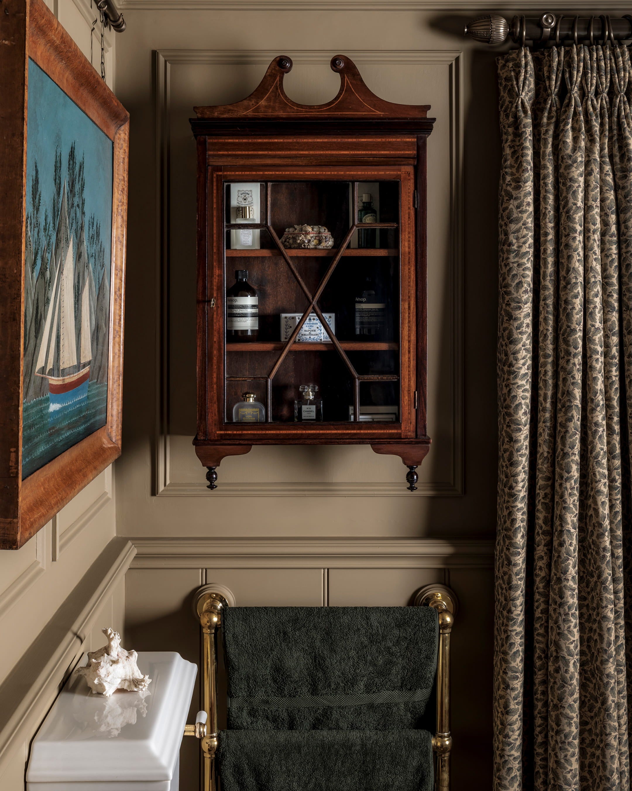 Antique mahogany cabinet with glass doors displaying curated items, fluted plaster walls in warm taupe and patterned drapery