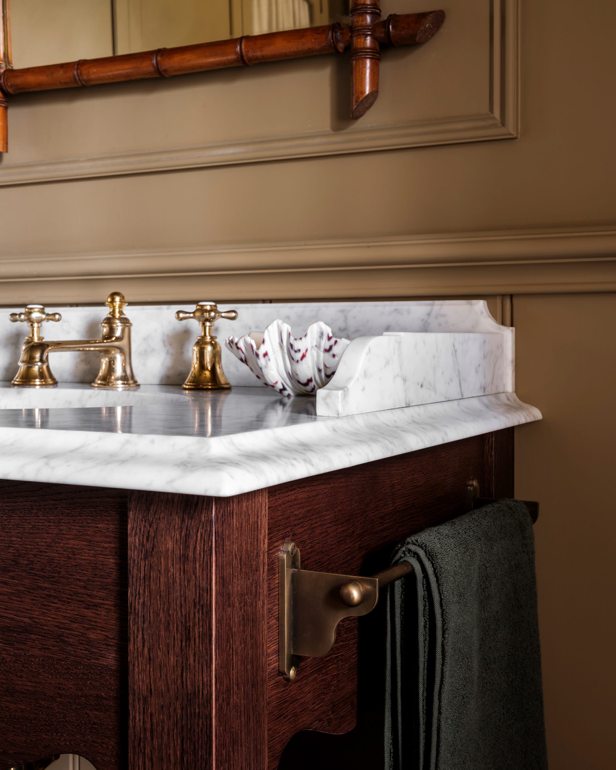 Bathroom vanity featuring a white marble countertop, dark walnut cabinetry, and antique brass faucets with a textured towel holder