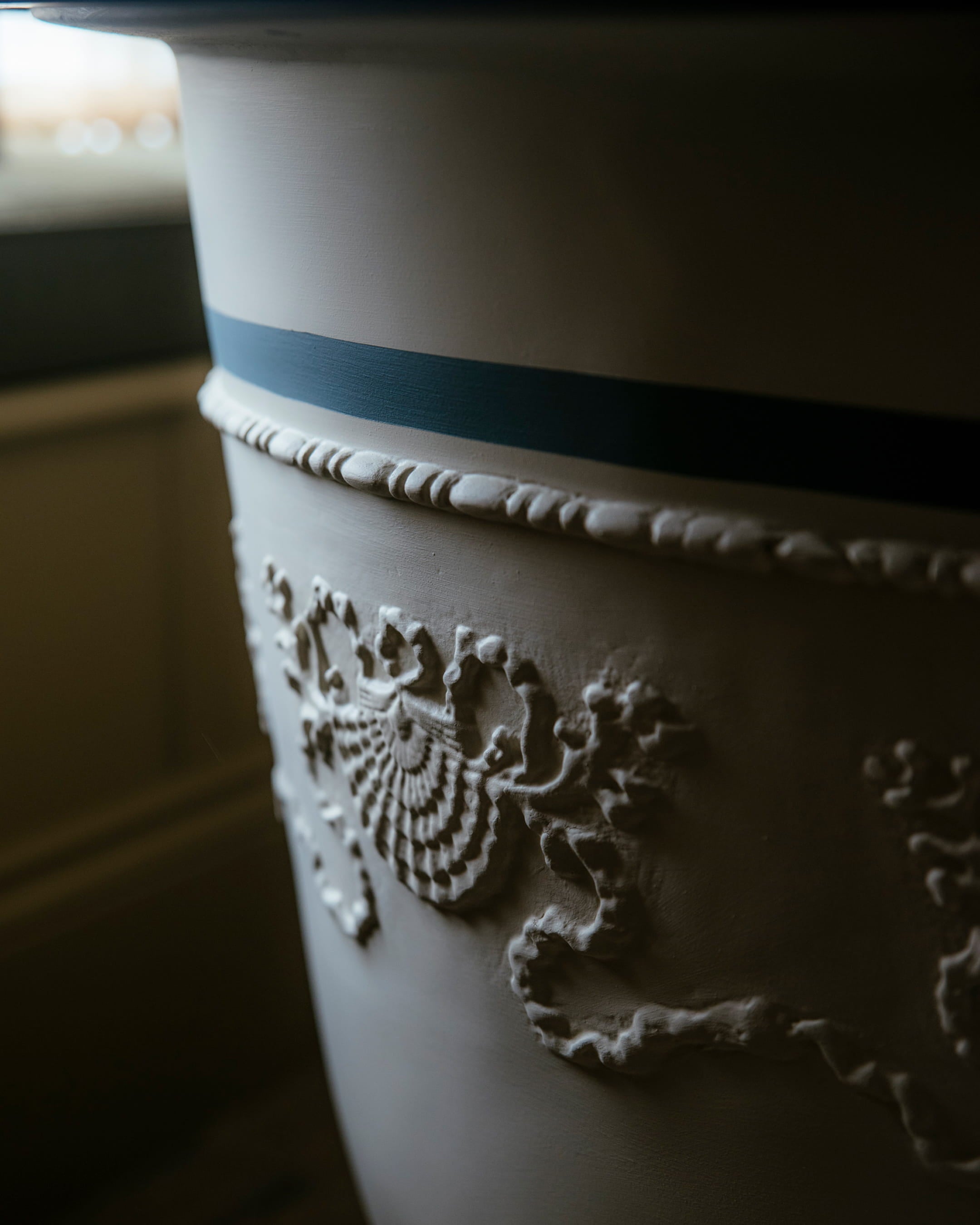 Close-up of a decorative plaster column featuring intricate shell motifs and a subtle blue stripe against a warm ivory background