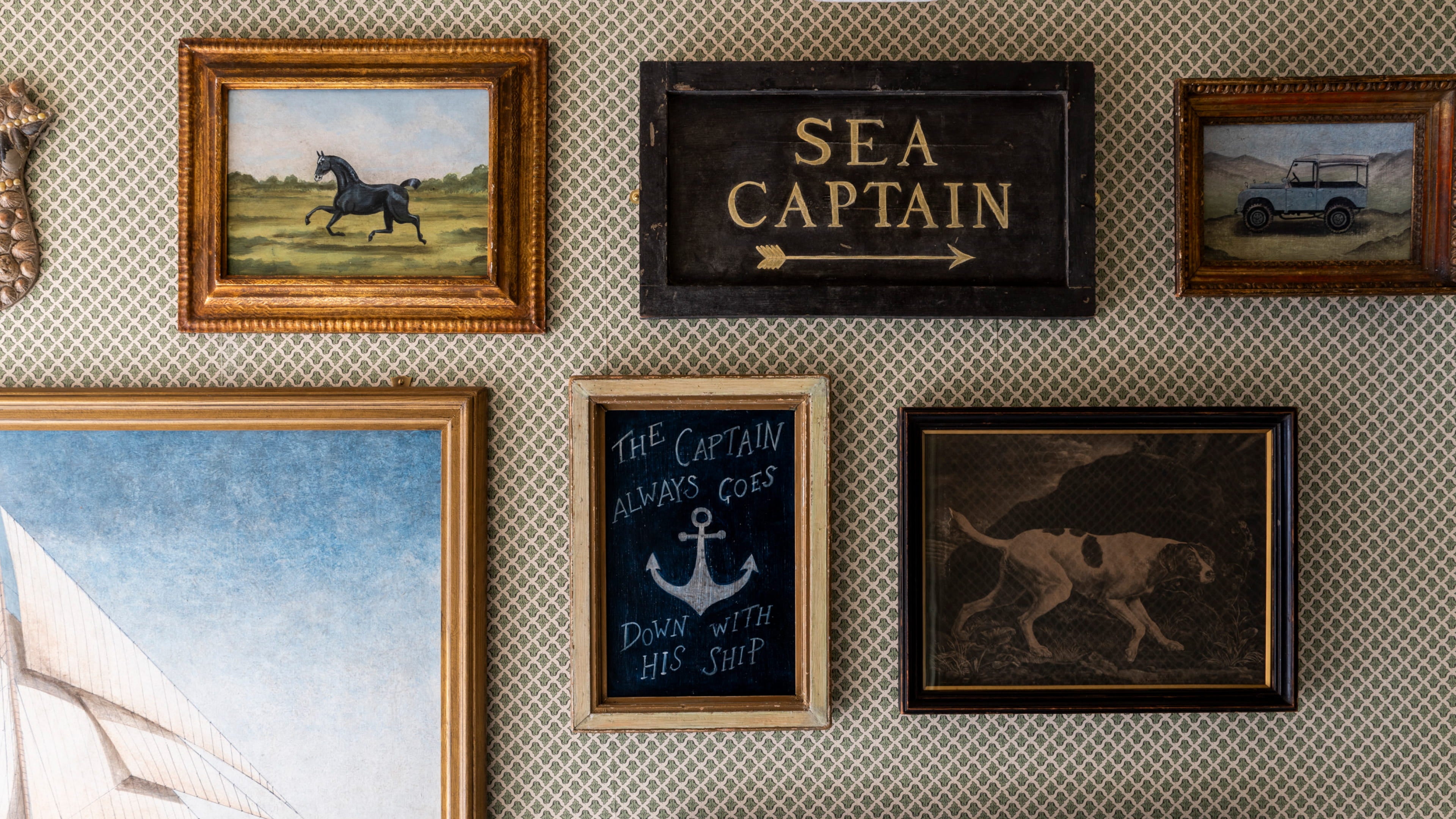 Gallery wall featuring vintage artwork in ornate frames, including a horse, a dog, and a nautical sign, against patterned wallpaper