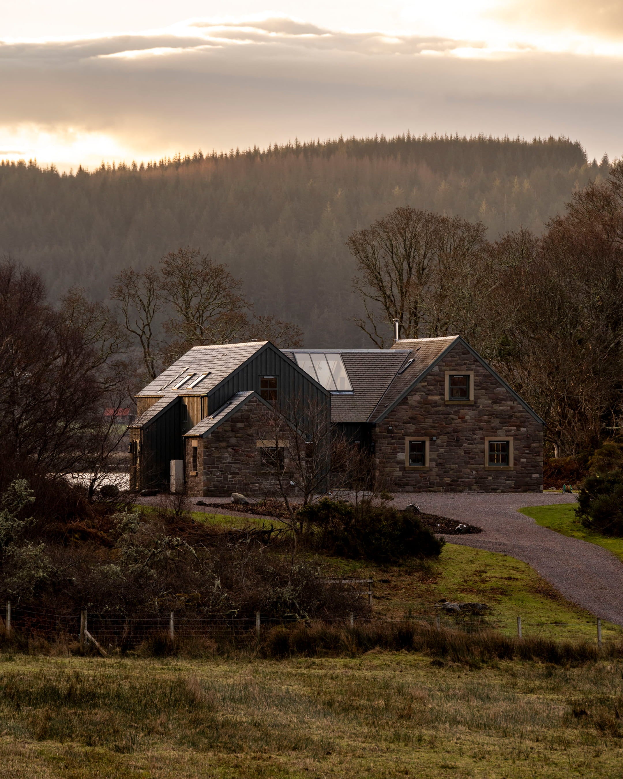 Contemporary stone house with dark timber cladding, large windows, and a slate roof nestled in a serene landscape