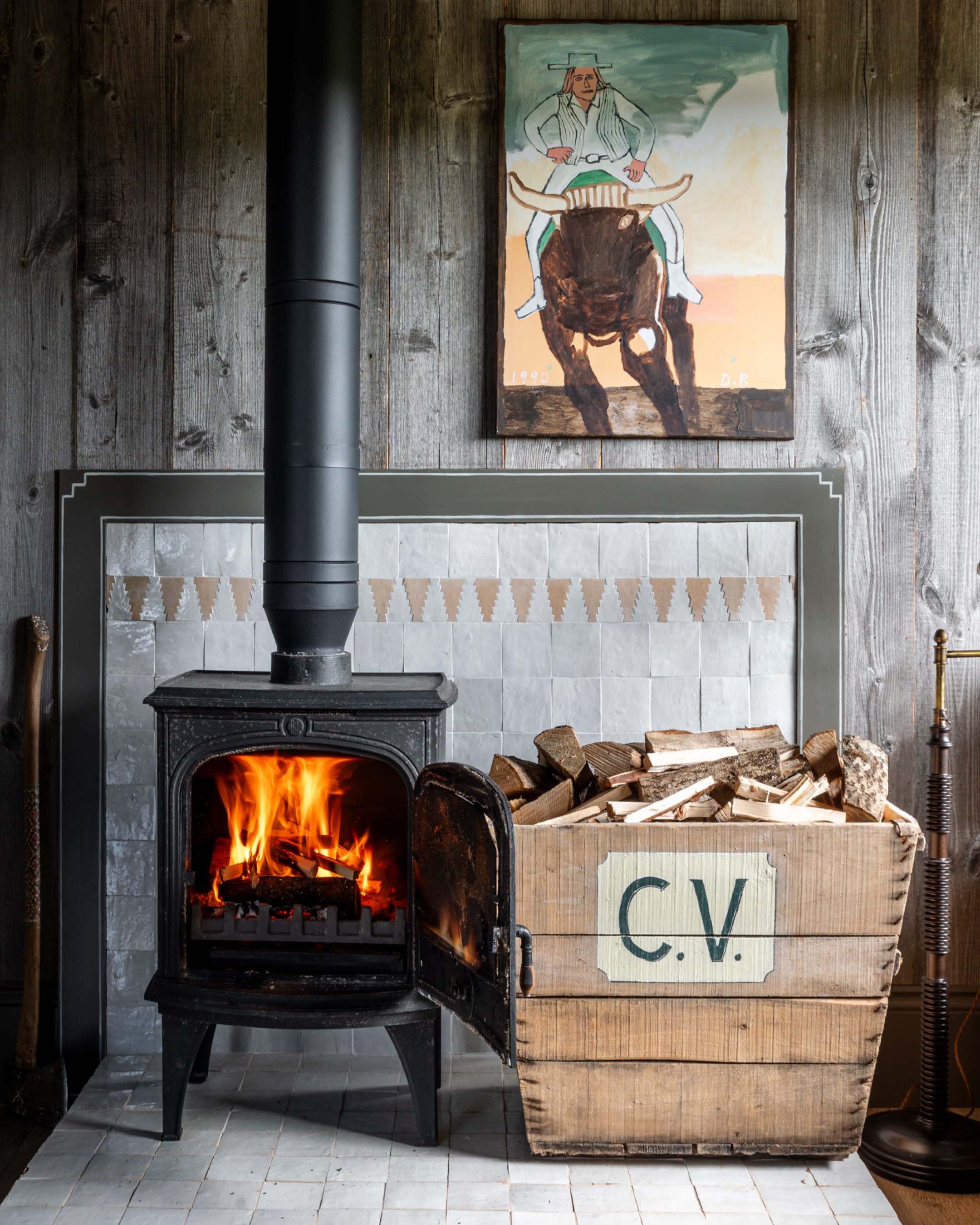 Cozy living space featuring a black cast iron stove, light grey tiled surround, and a wooden log basket with a vintage label