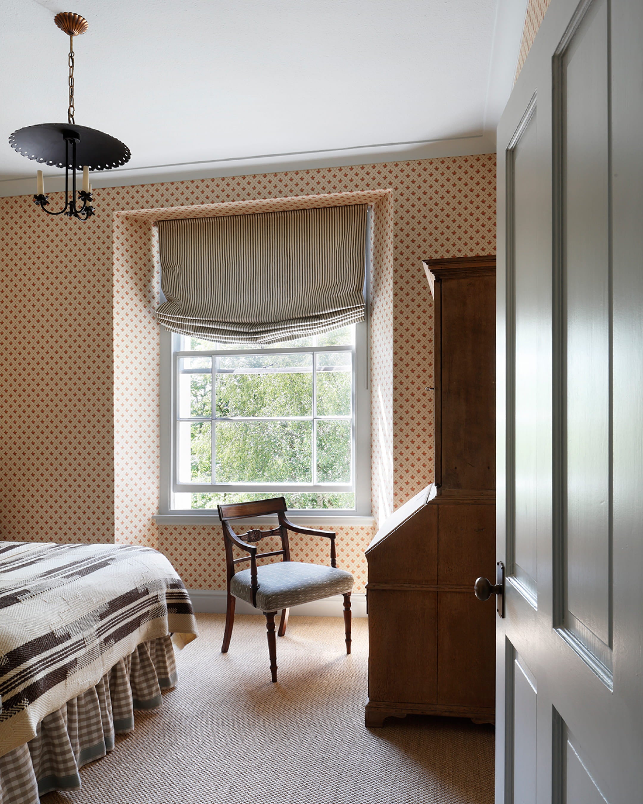 Cozy bedroom featuring soft coral patterned wallpaper, a vintage oak writing desk, and a light grey upholstered chair