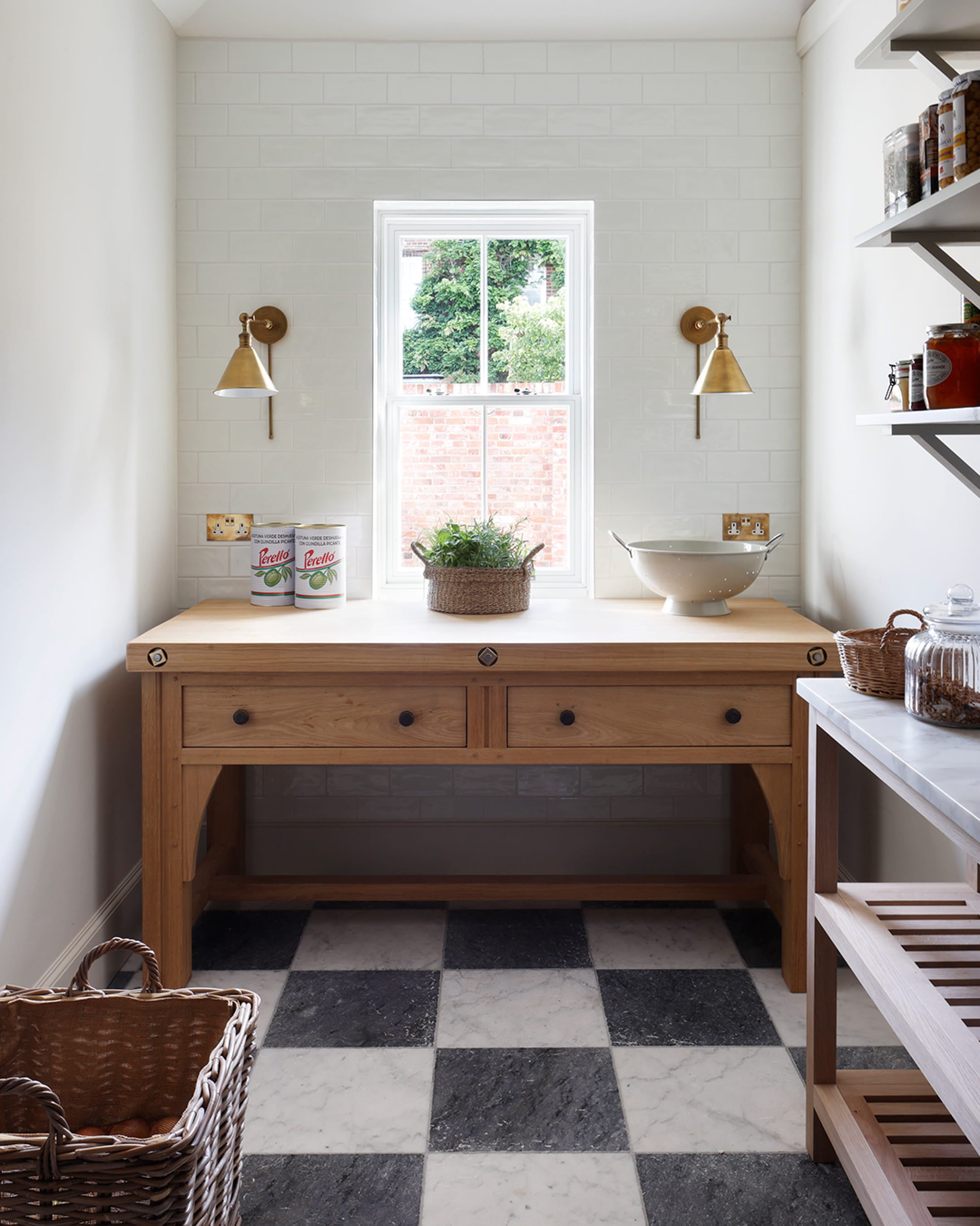 Bright kitchen featuring a wooden worktable, black and white checkered marble floor, and brass wall sconces with a view of greenery outside