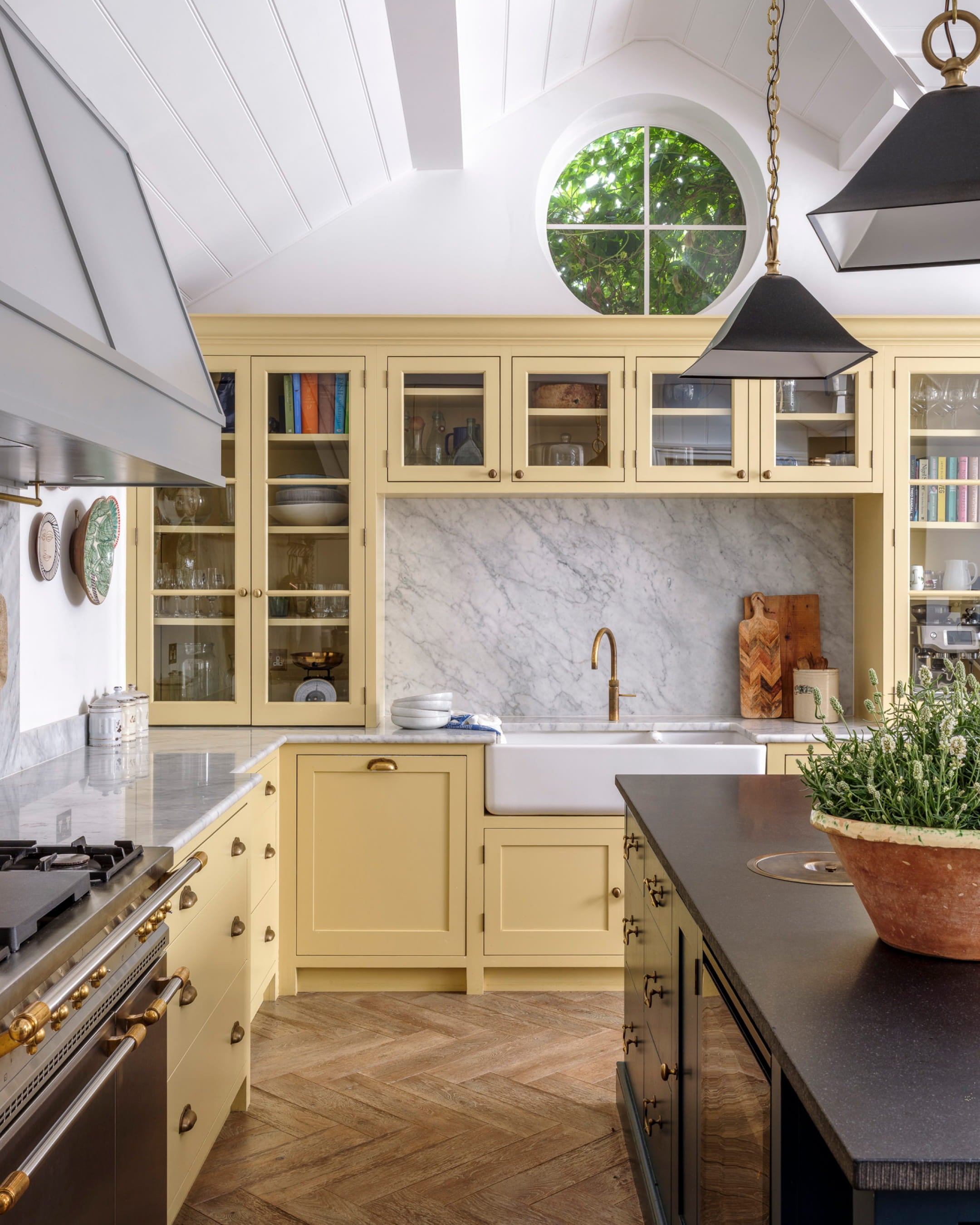 Bright yellow cabinetry contrasts with a dark stone island, featuring a marble backsplash and herringbone oak flooring