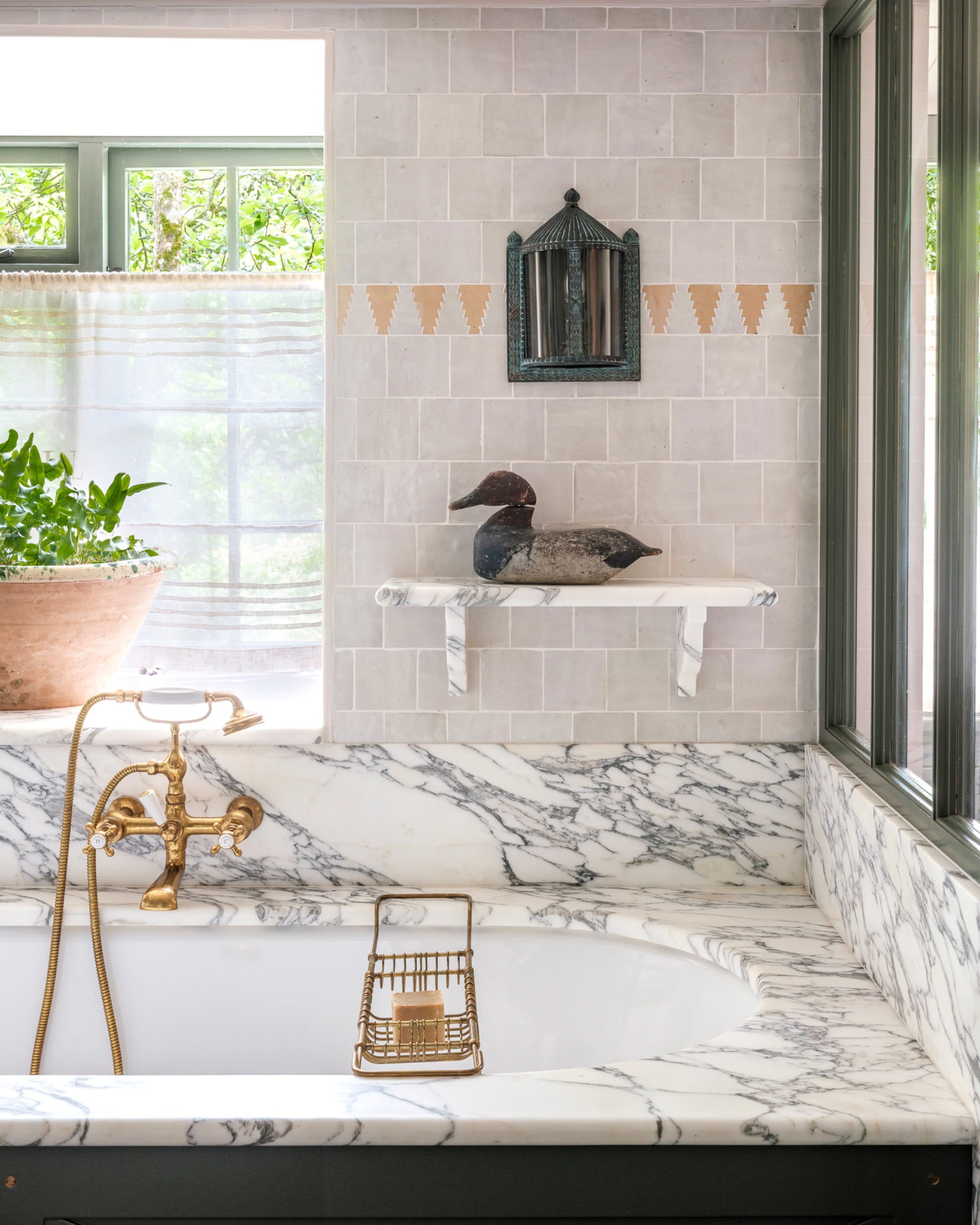 Bathroom featuring a freestanding bathtub with a white marble surround, pale grey tiled walls, and a vintage brass faucet