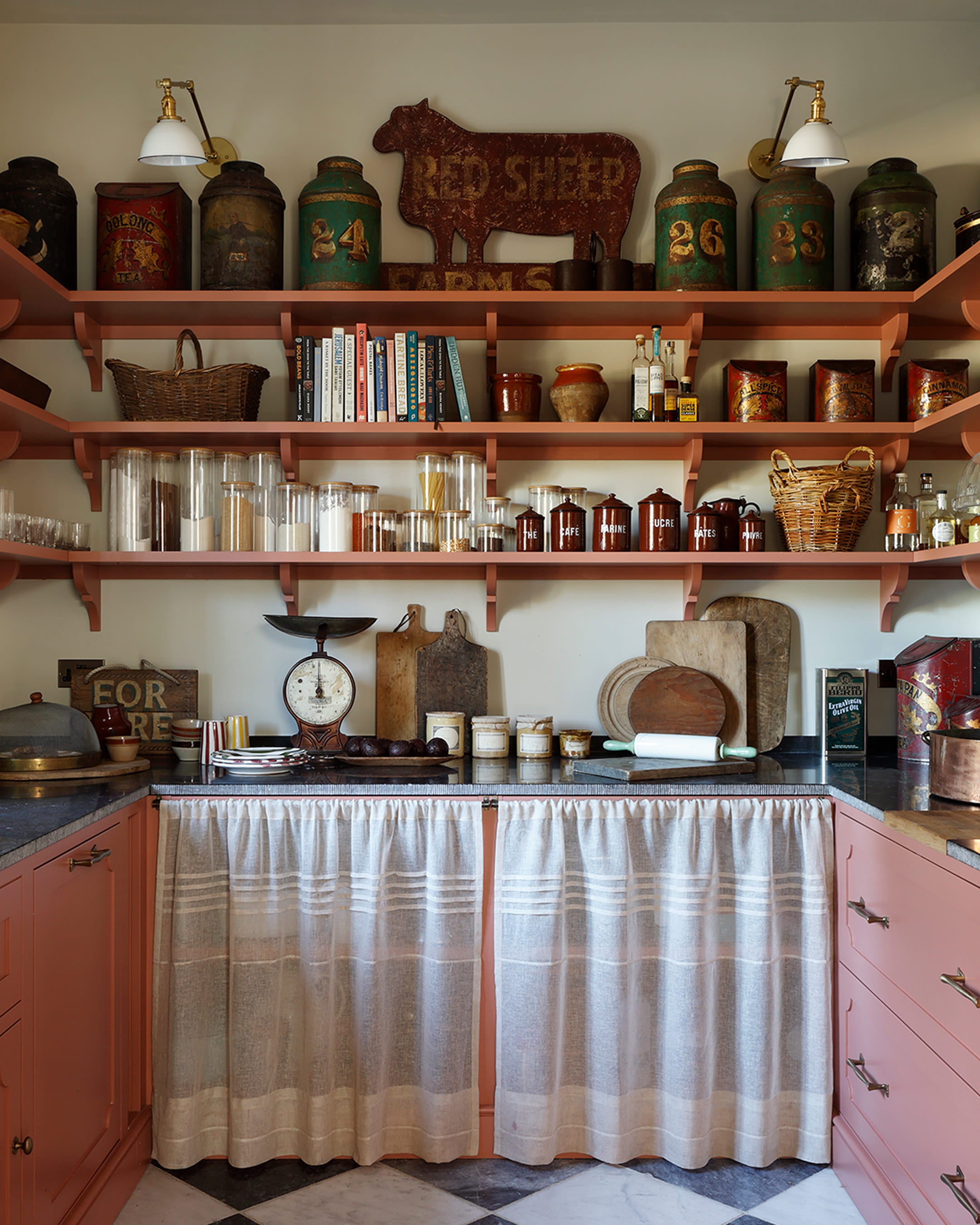 Rustic kitchen with coral pink cabinetry, marble countertop, vintage glass jars, and eclectic wall-mounted decor including a cow sign