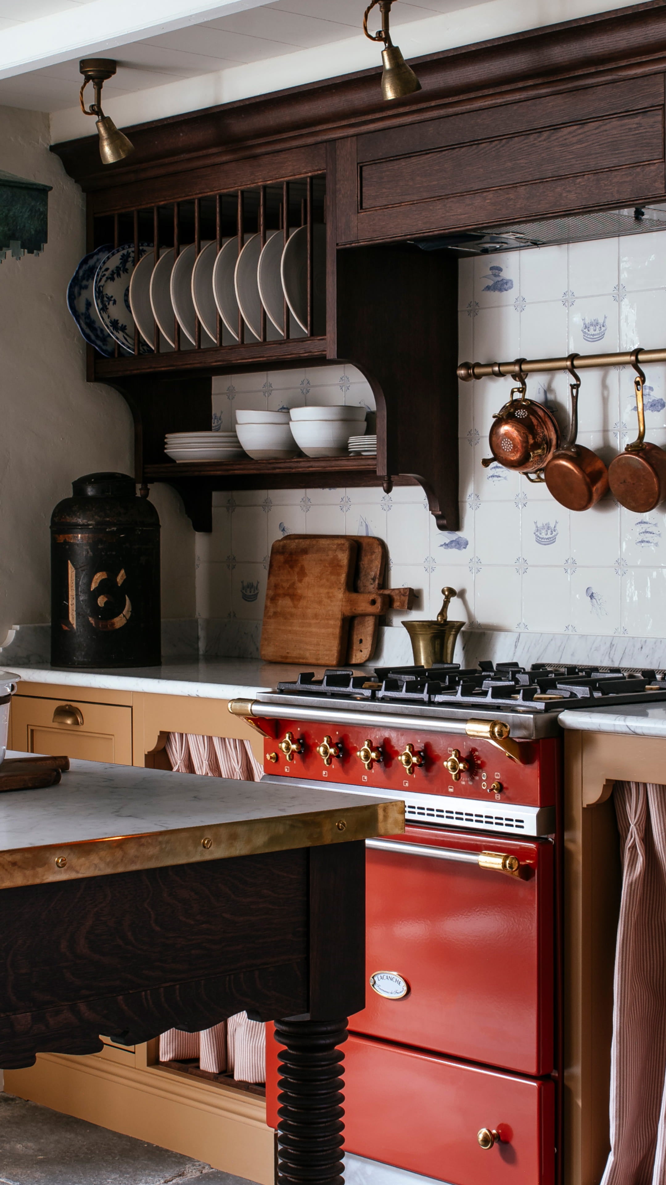 Kitchen featuring a brass range cooker, white ceramic dishware, and dark oak cabinetry with a vintage copper pot collection