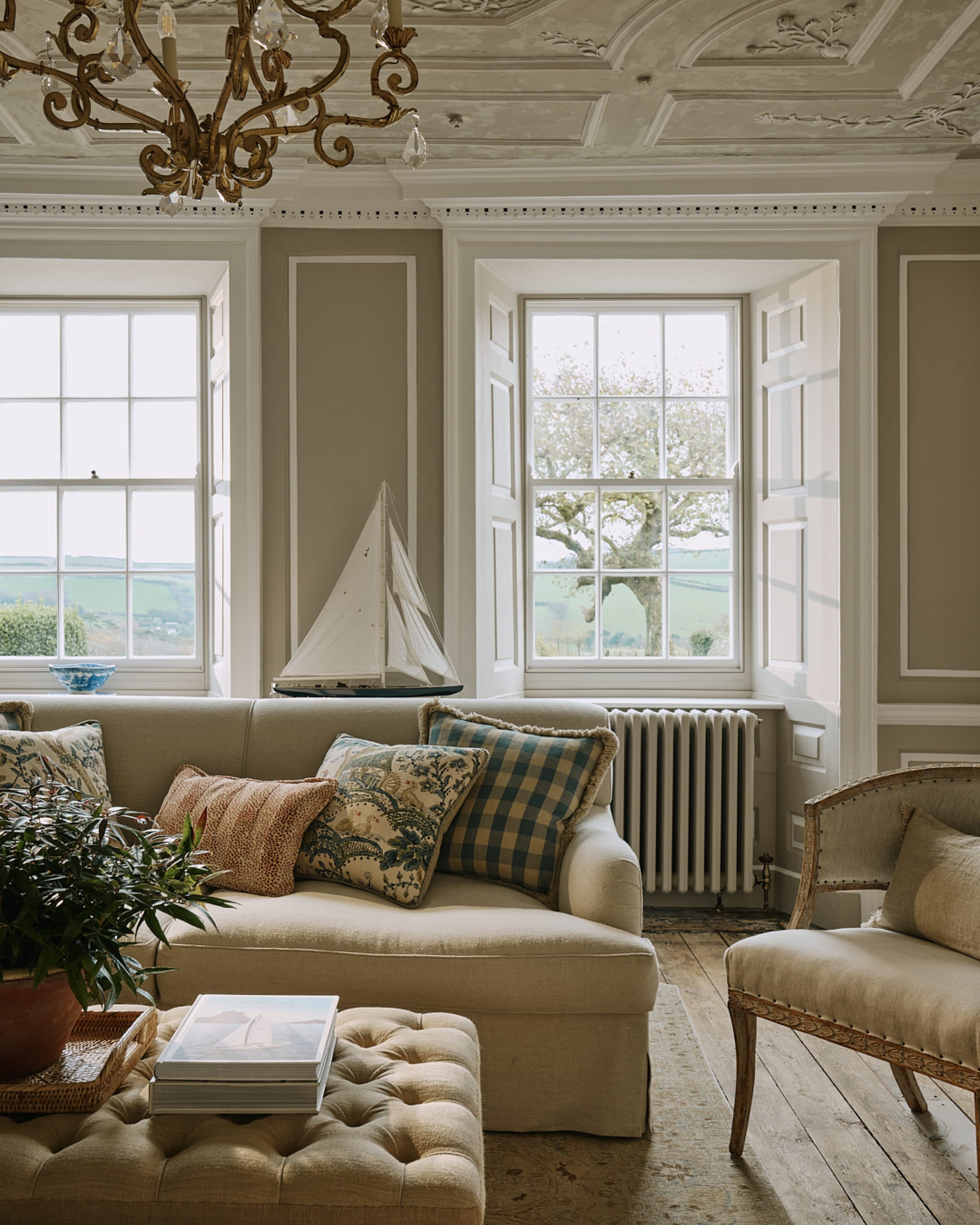 Cozy living room featuring a linen sofa with patterned cushions, herringbone oak flooring, and a vintage tufted ottoman