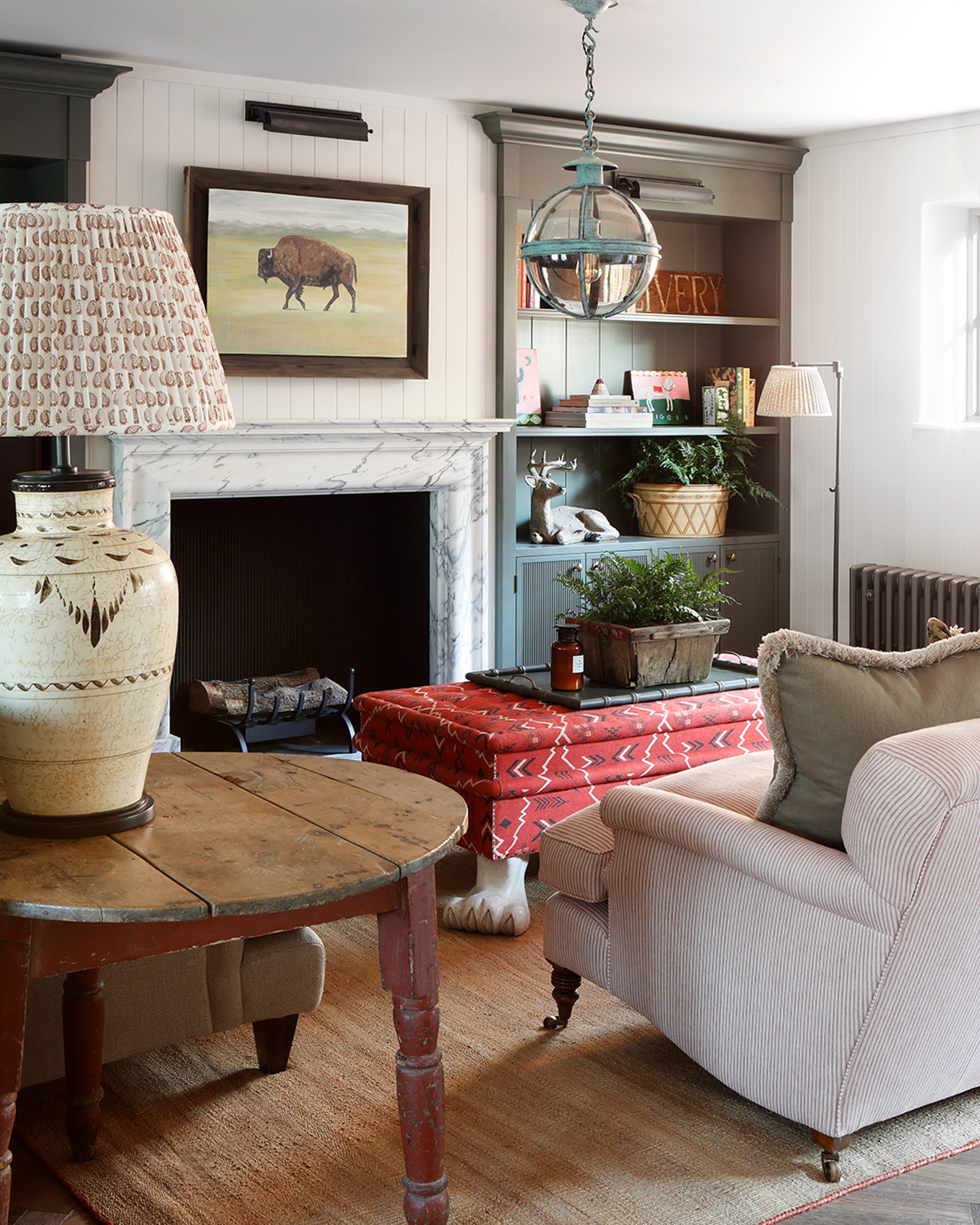 Cozy living room featuring a fluted plaster fireplace, a rustic wooden table, and a vibrant red patterned ottoman