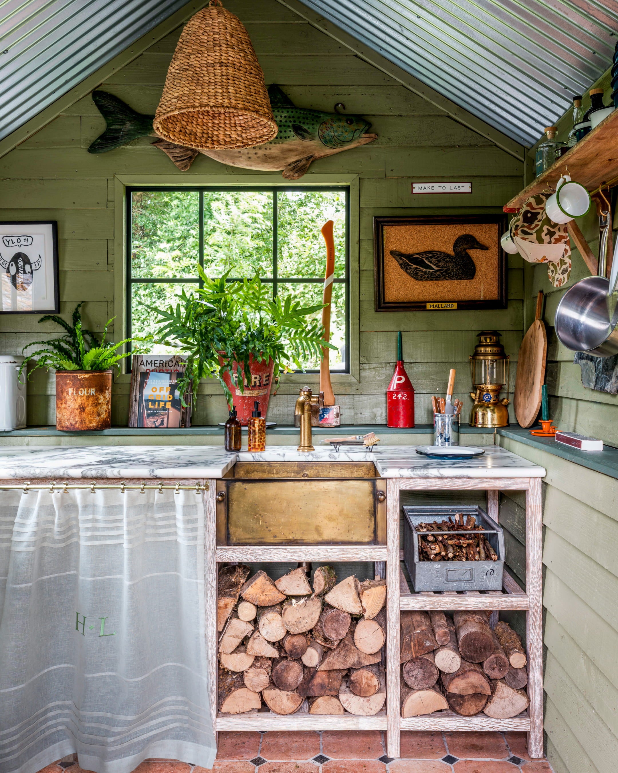Rustic kitchen featuring green shiplap walls, a marble countertop, brass fixtures, and a woven pendant light above the sink