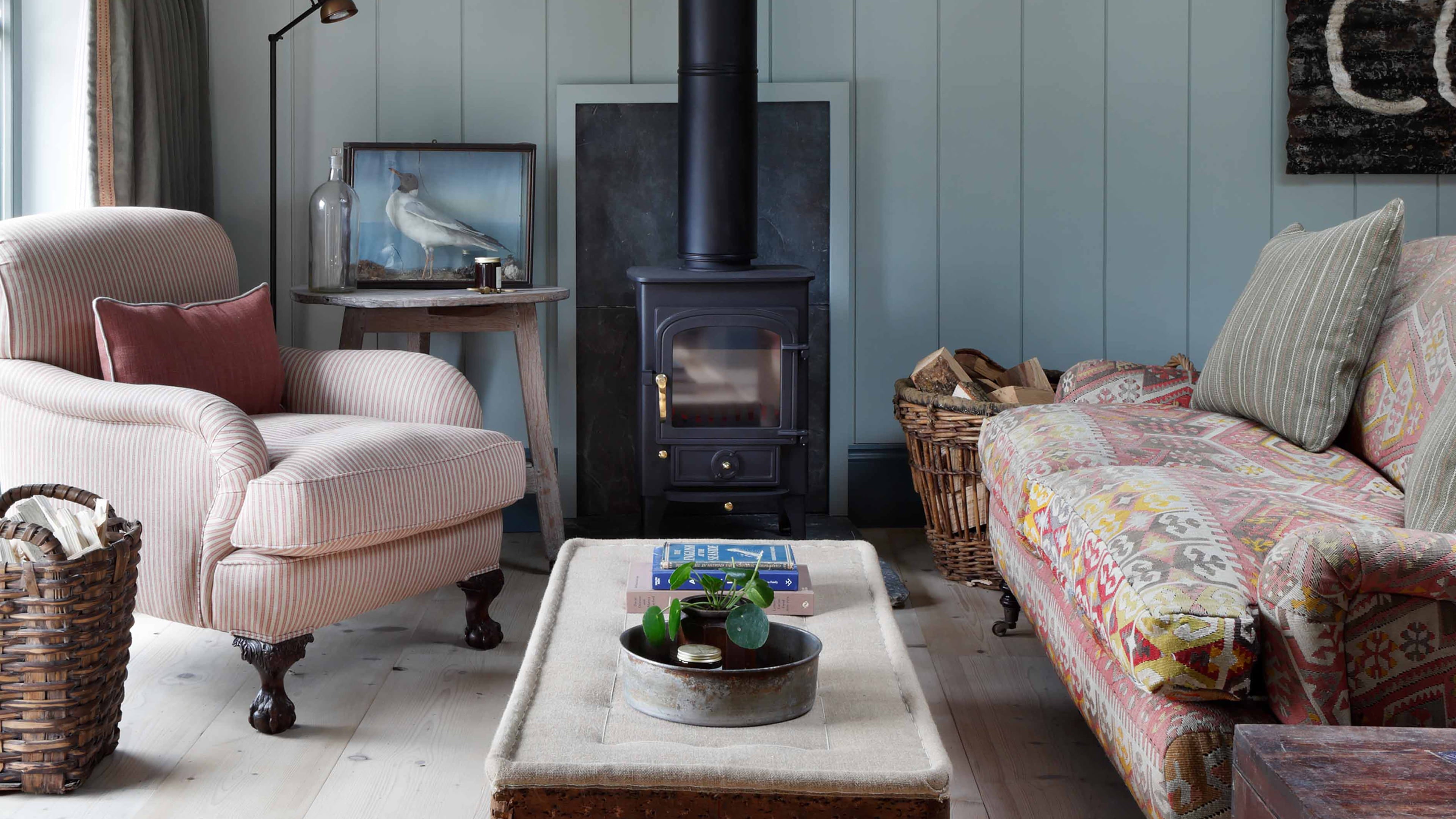 Cozy living area featuring a pale blue wood-paneled wall, a black wood-burning stove, and a patterned upholstered sofa