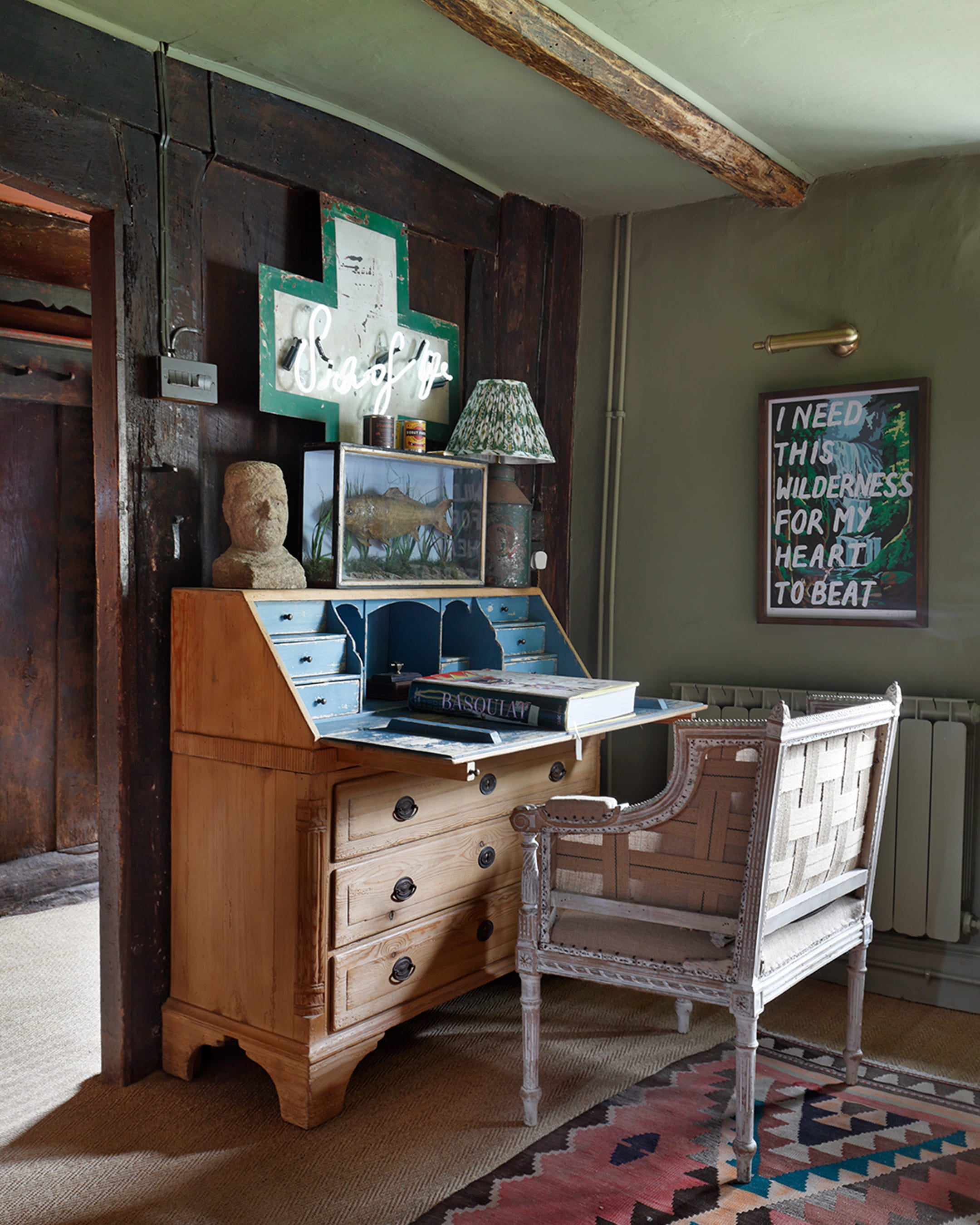 Corner workspace featuring a vintage oak desk with blue accents, a woven chair, and a colorful patterned rug on a herringbone floor