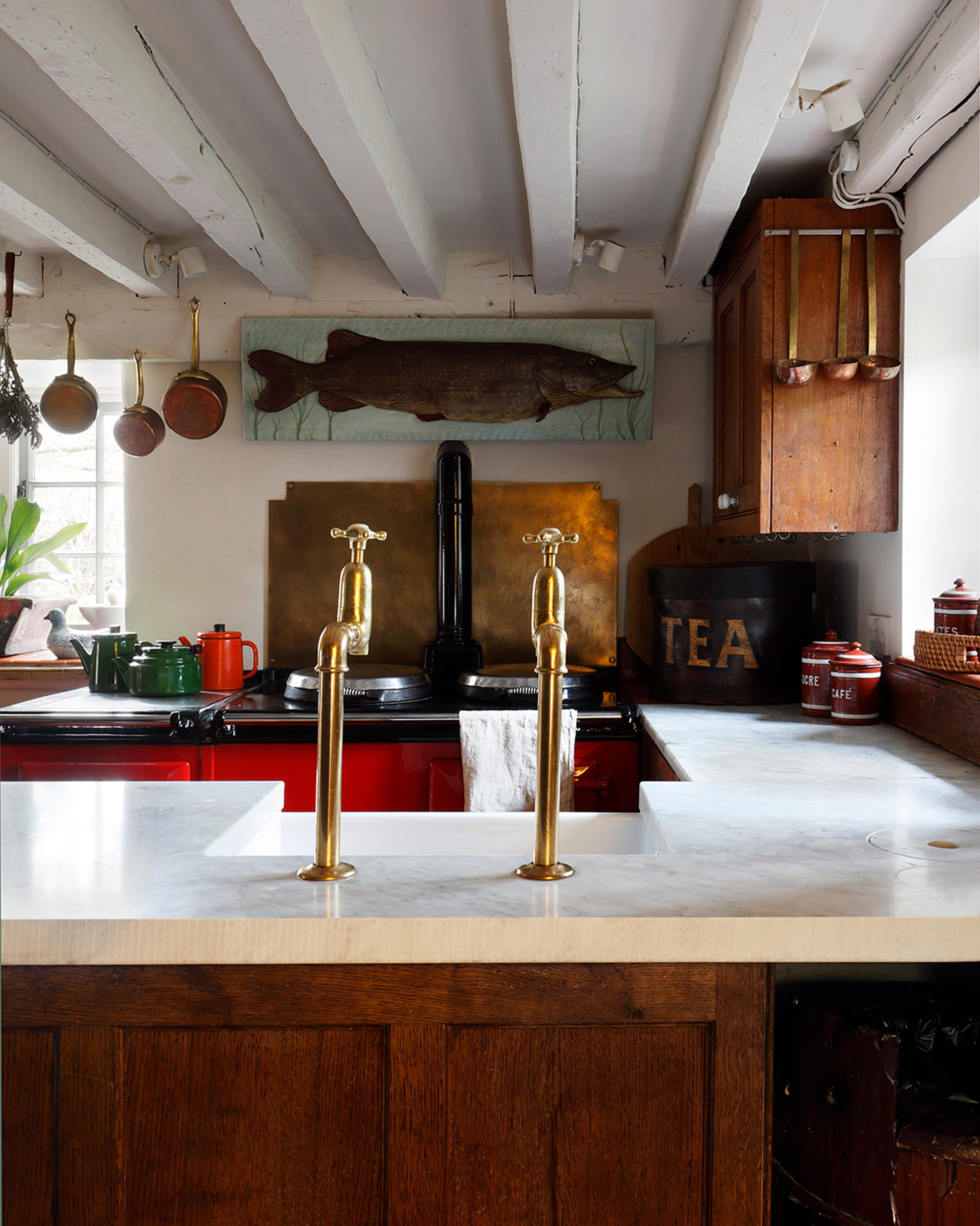 Rustic kitchen featuring a white marble countertop, dark walnut cabinetry, and vintage brass taps with hanging copper pots