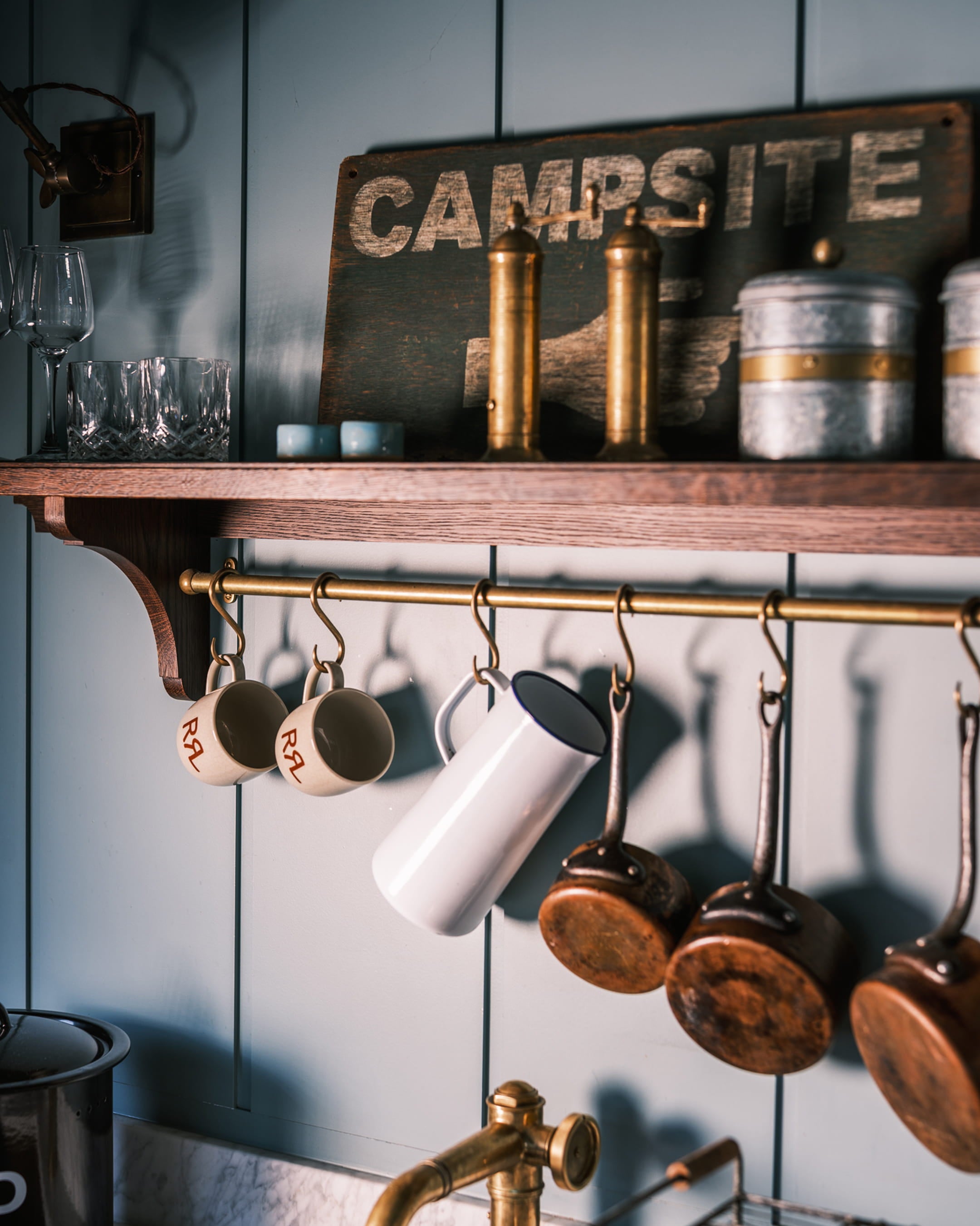 Open kitchen with soft blue paneling, a brass pot rack, and rustic copper cookware hanging above a marble countertop