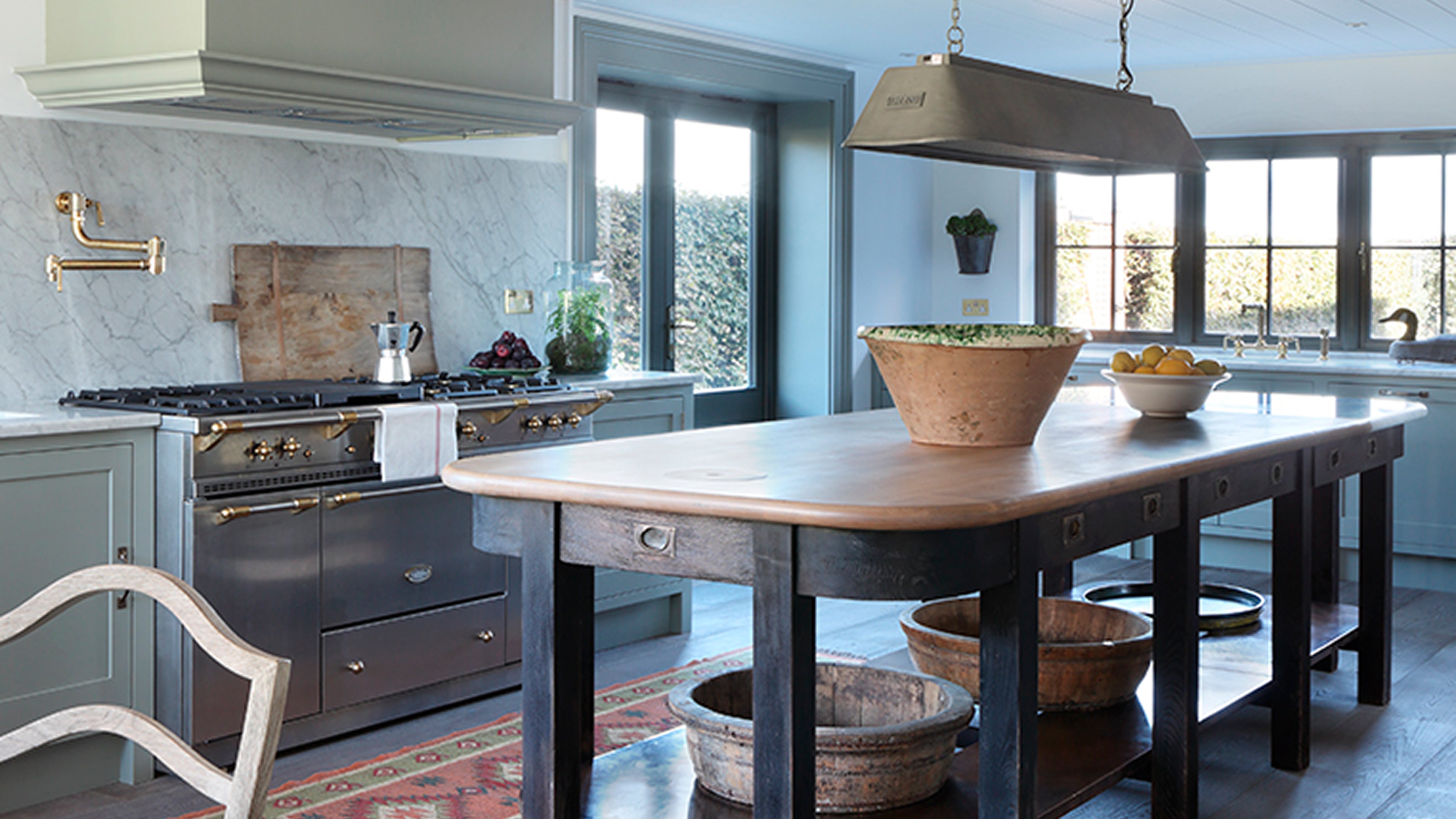 Modern kitchen featuring a large wooden island with a rounded edge, herringbone oak flooring, and marble backsplash with brass fixtures