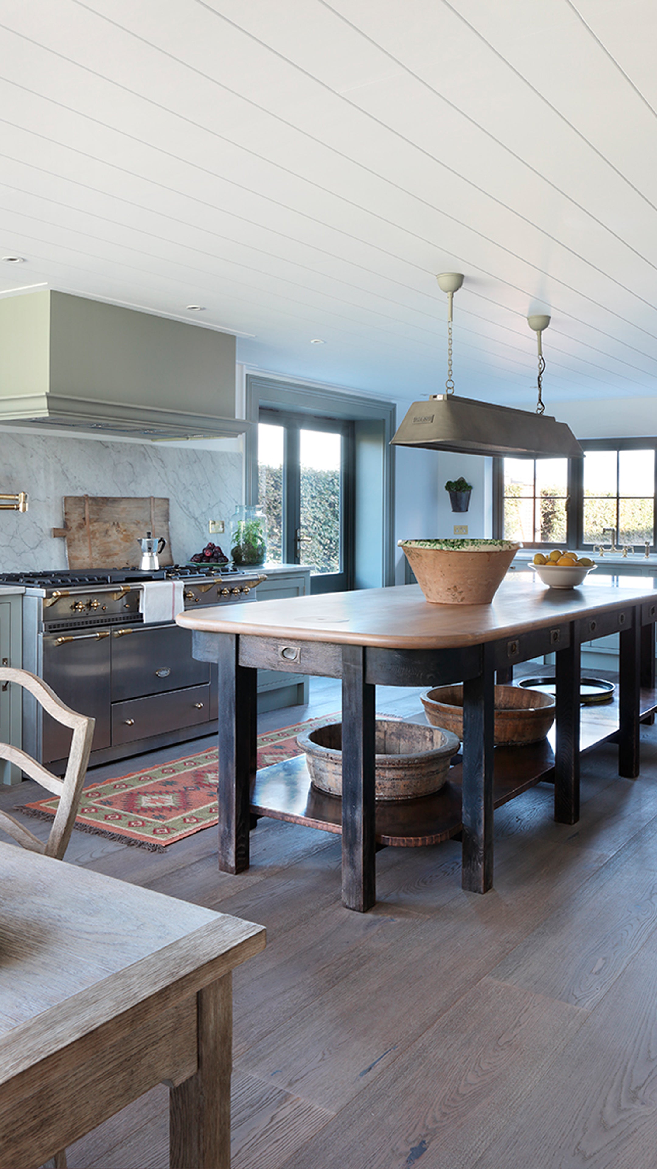 Contemporary kitchen featuring pale green cabinetry, a wooden island with rustic bowls, and a marble backsplash