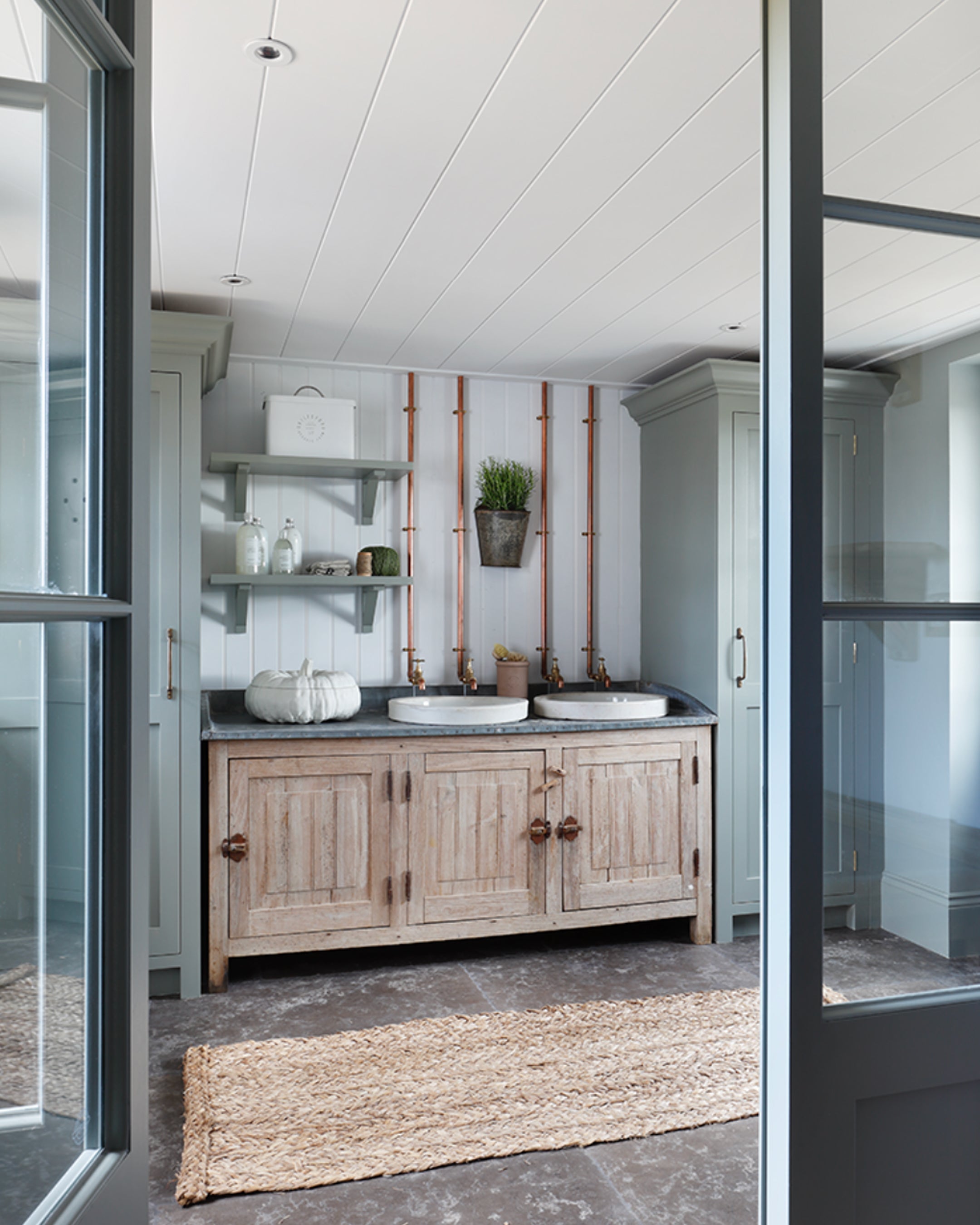 Bright bathroom featuring pale blue cabinetry, a dark granite countertop, and vintage wooden cabinetry with copper piping accents